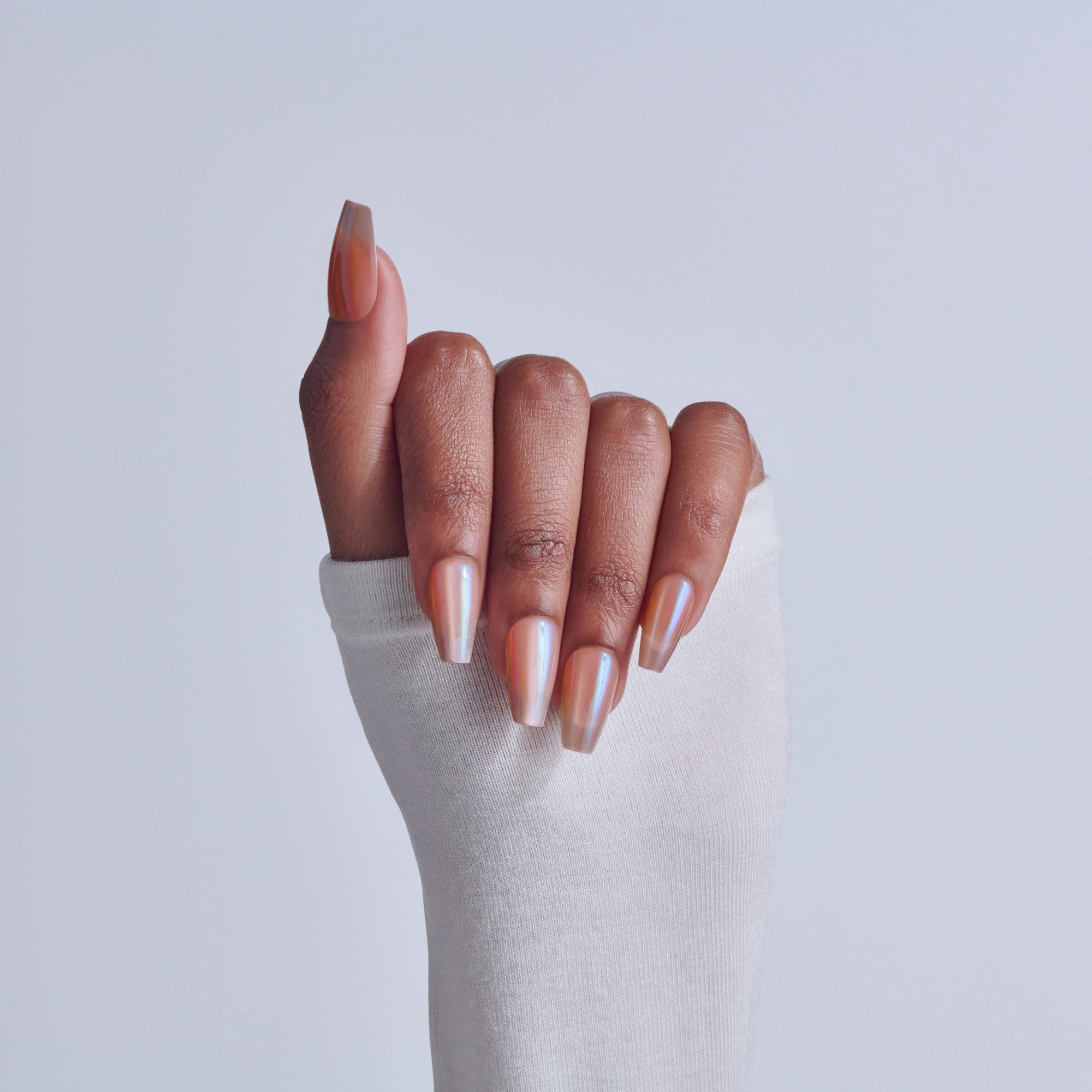 Hand with pearlescent manicure nails in pink and white ombre finish on white sleeve.