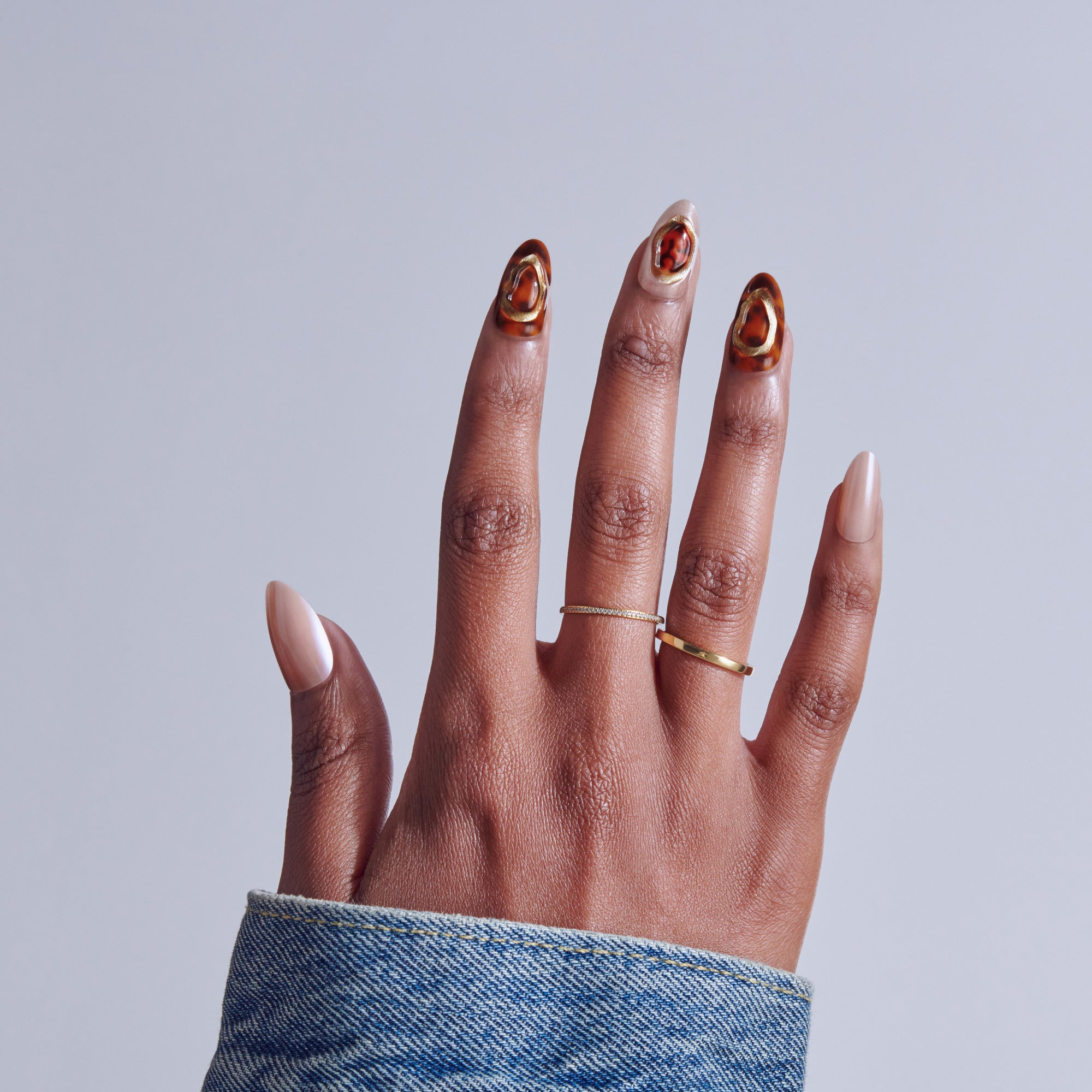 Hand displaying manicure with red and gold nail art and gold rings against gray background.