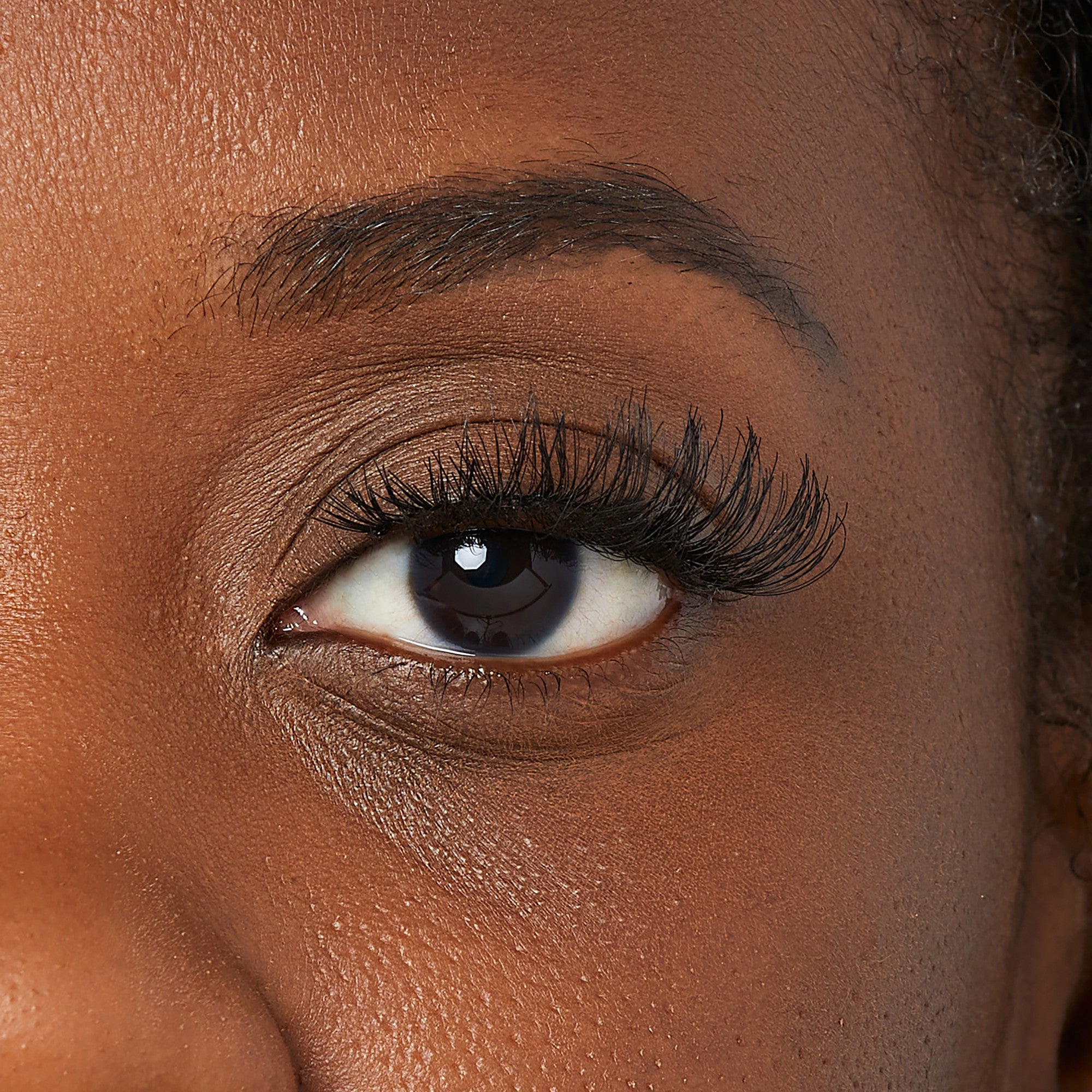 Close-up of a dark-skinned eye wearing KISS So Wispy false eyelashes in the Pixie style, showing natural, voluminous, and wispy lash appearance.