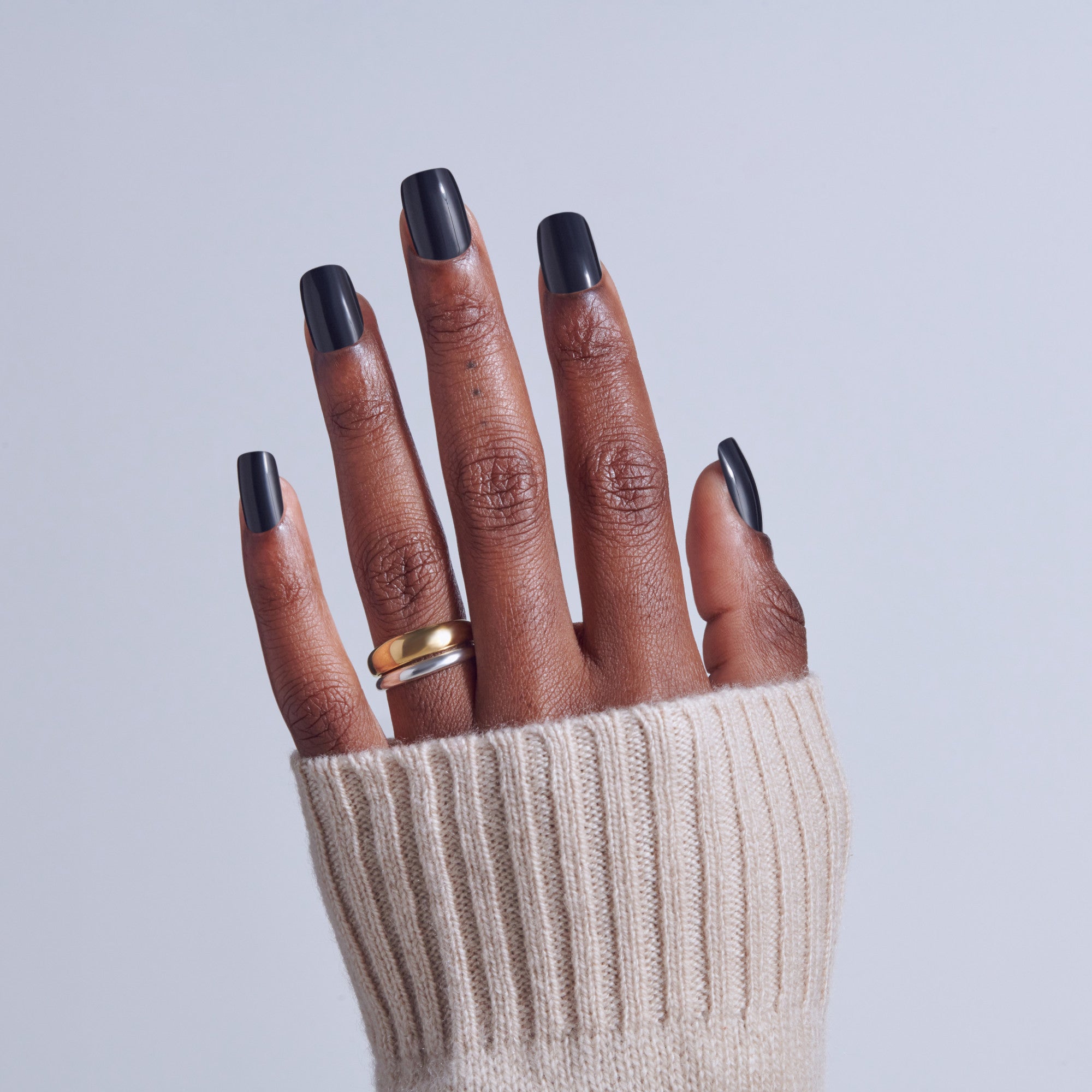 Hand with black ombre nails and gold ring, wearing cream ribbed sweater.
