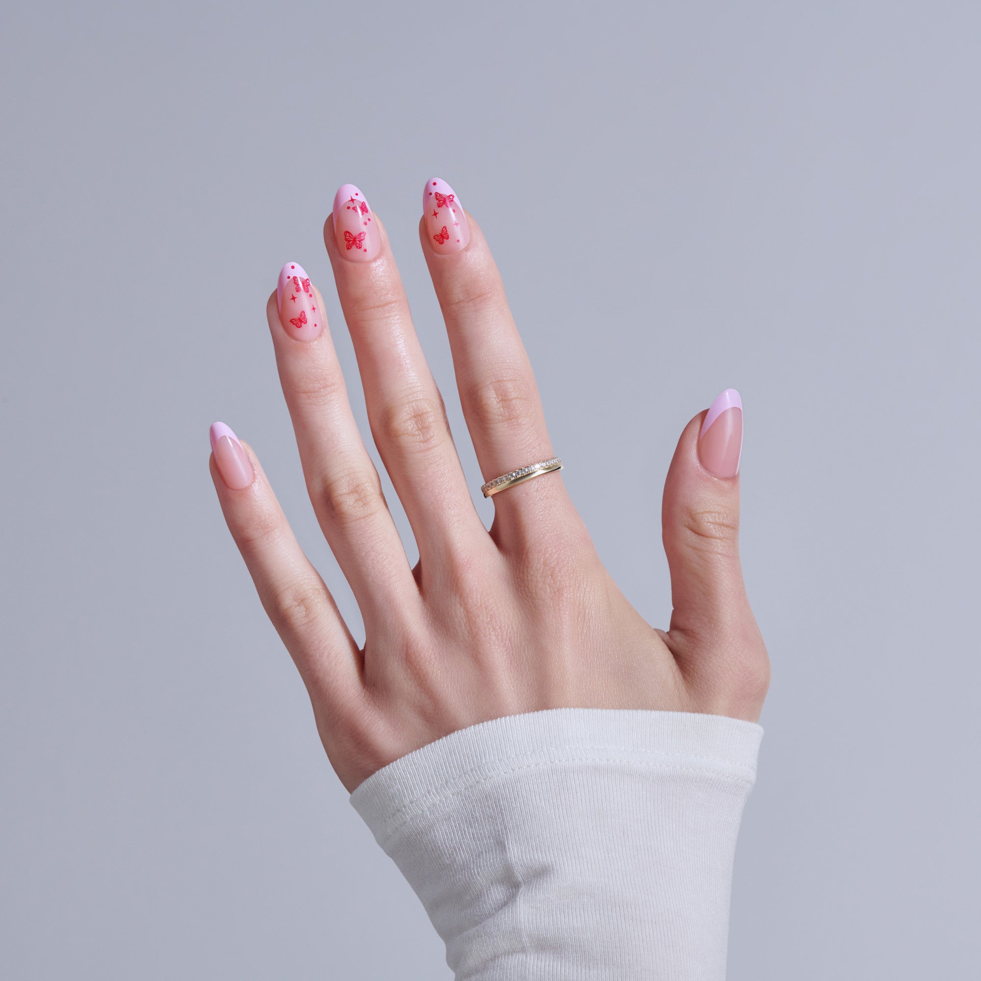 Hand displaying pink butterfly nail art with diamond ring on white sleeve background