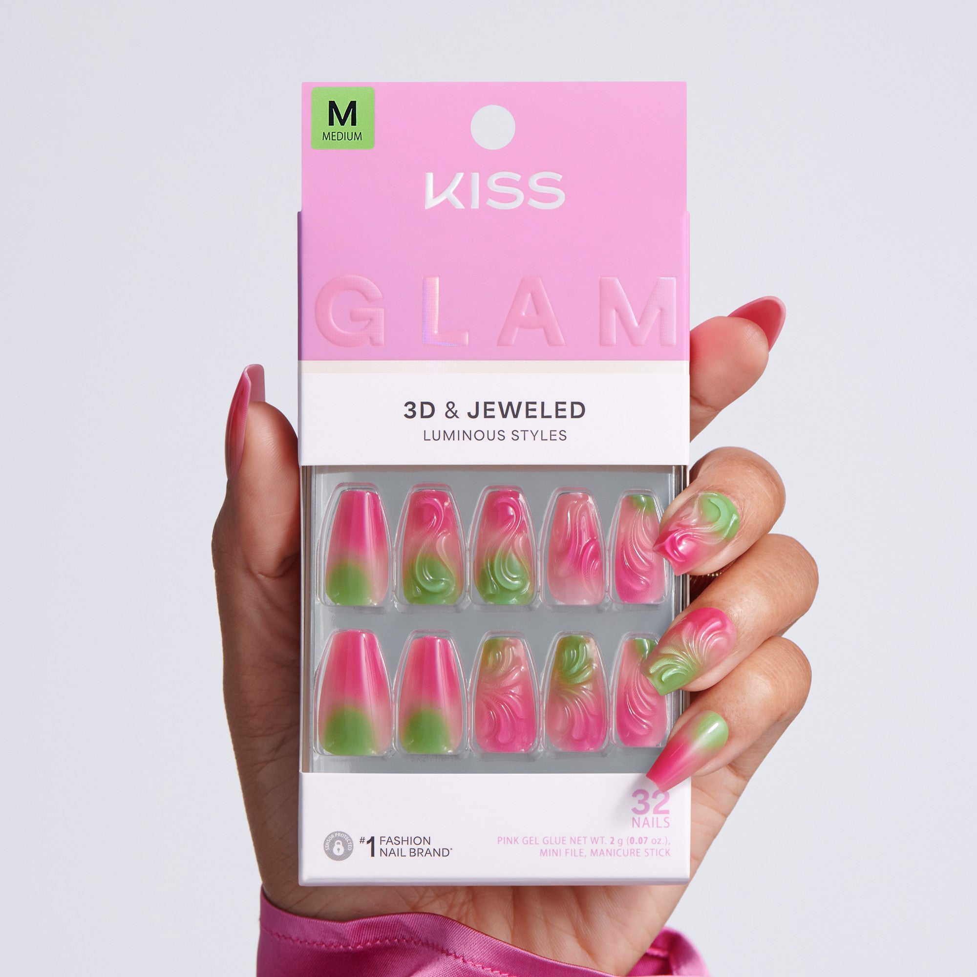 Hand holding KISS Glam 3D & Jeweled Luminous Styles press-on nails packaging, Medium size, 32 nails, pink and green ombre coffin nails on light gray background