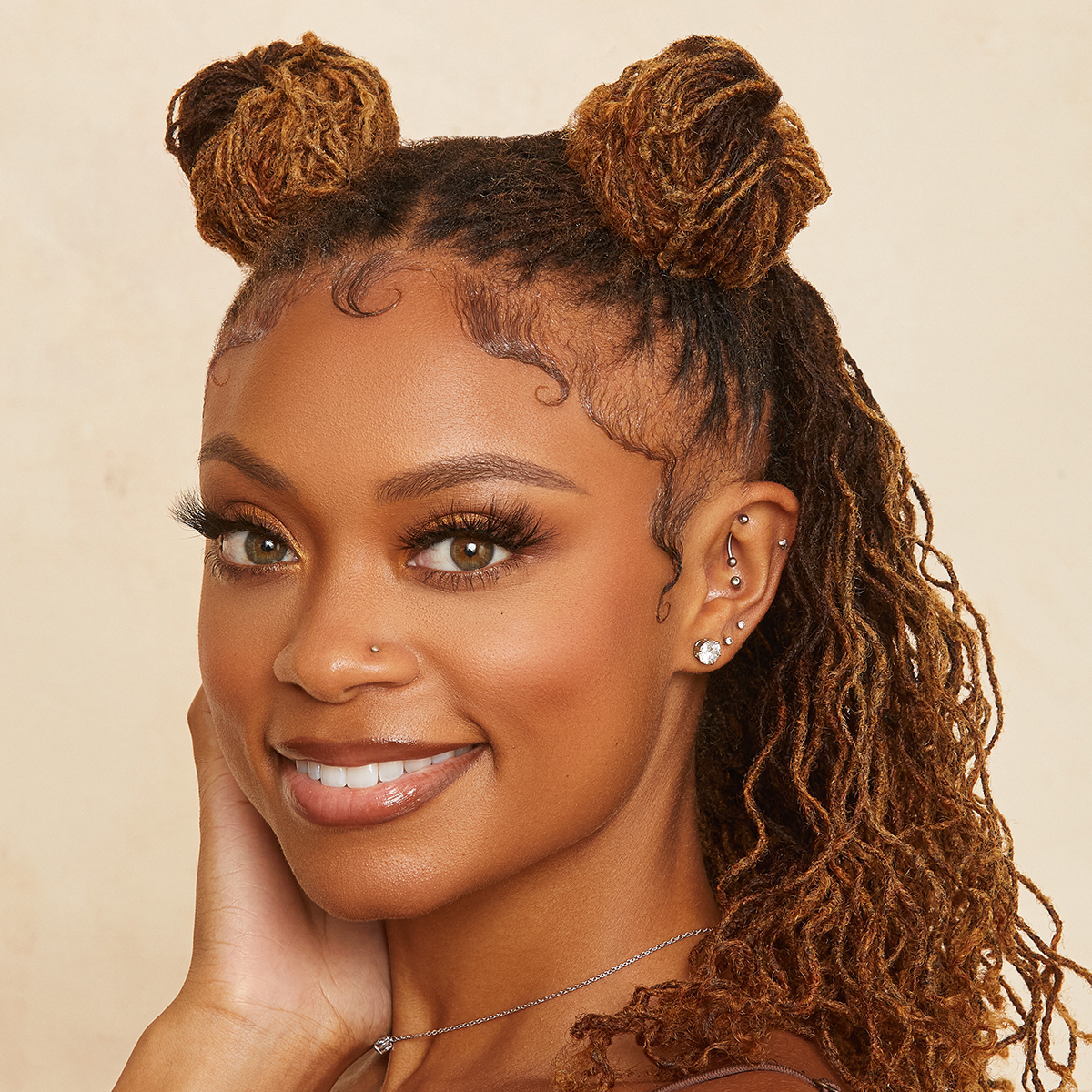 Close-up of a smiling woman with styled edges and two peach-colored hair buns, showcasing smooth, defined baby hairs likely styled with edge fixer.