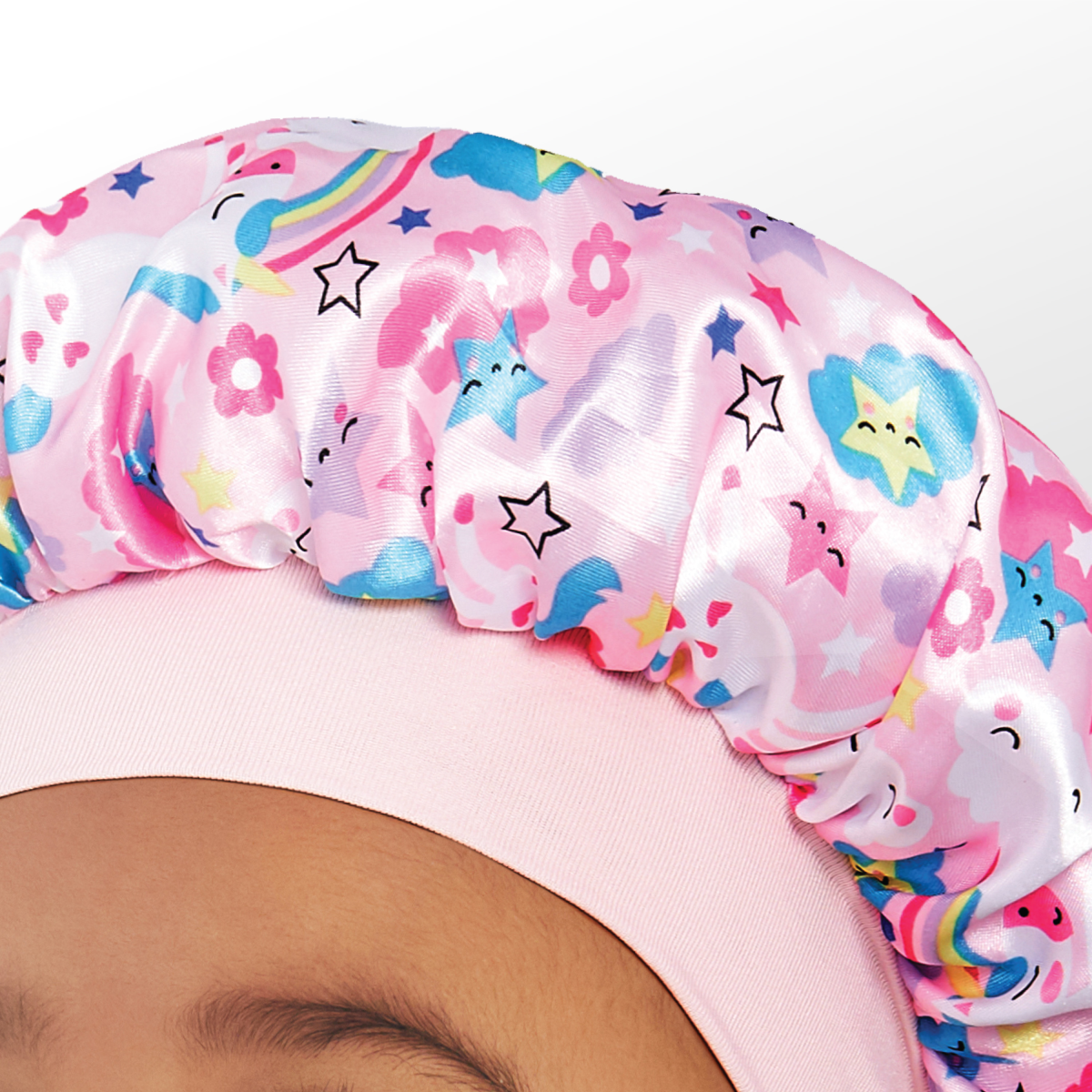 Toddler wearing a pink silky satin bonnet with colorful smiling stars, flowers, clouds, and rainbows pattern on fabric.