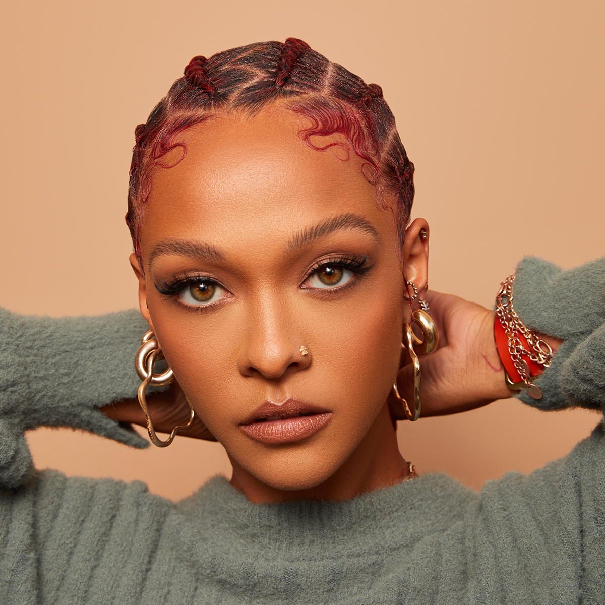 Close-up of a woman with tightly braided red hair and styled baby edges, wearing gold hoop earrings and a green fuzzy sweater, showcasing smooth, glossy hair edges.