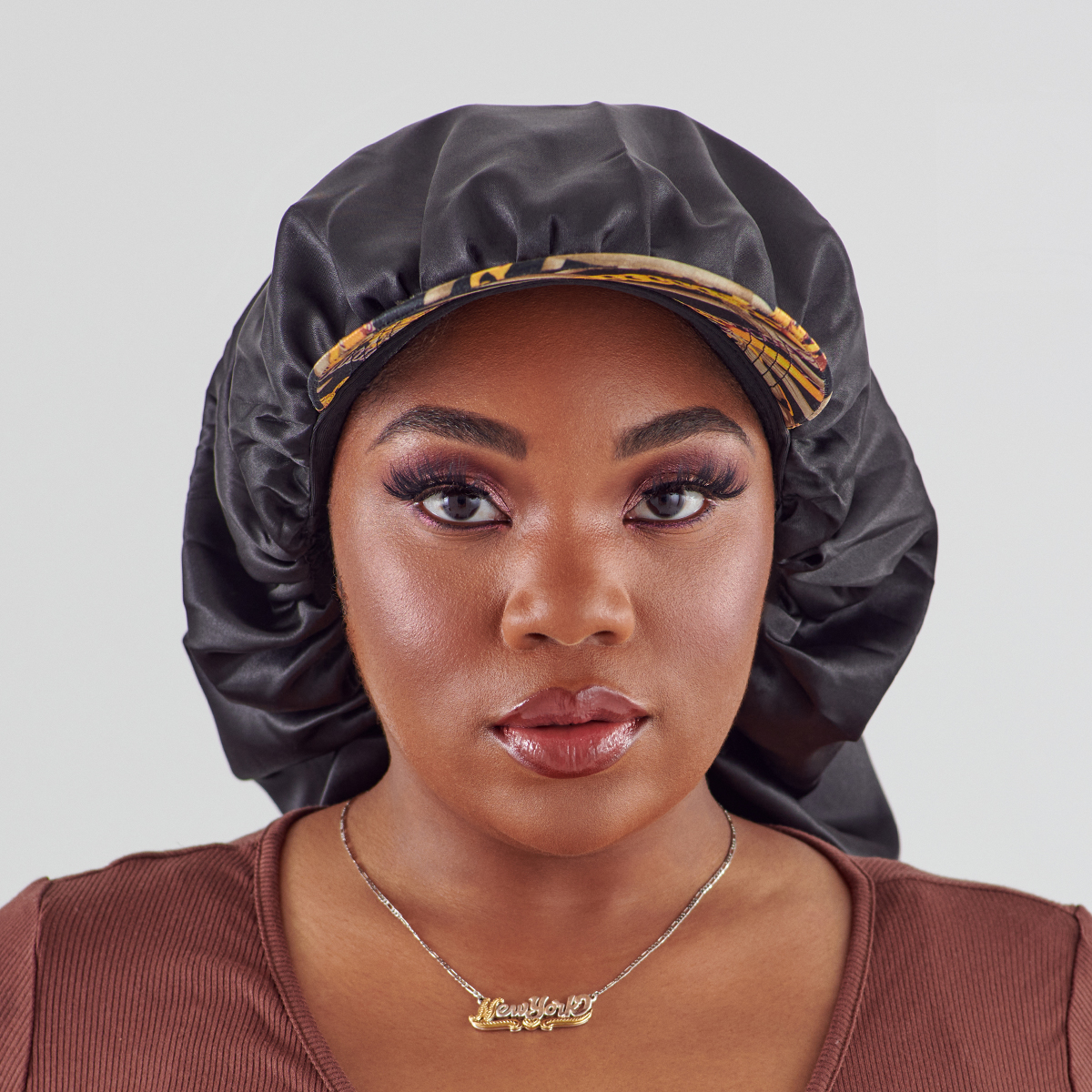 Close-up view of a woman wearing a black silky satin bonnet cap with a colorful patterned visor, styled over her hair against a plain background.
