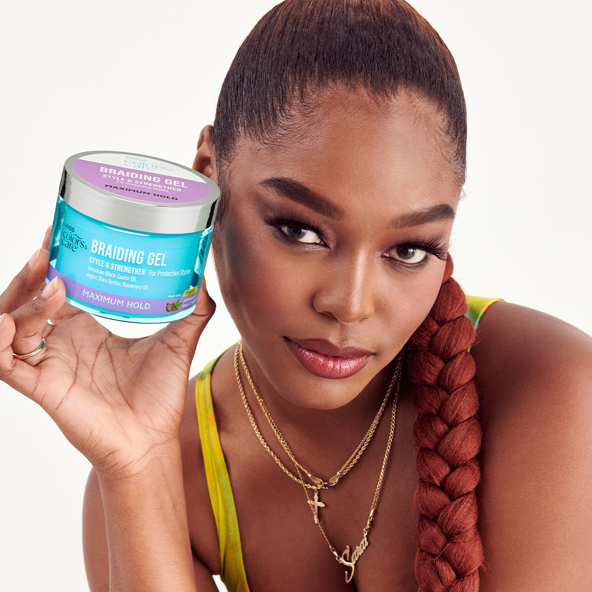 Woman with a long reddish braided ponytail holds a 6 oz. jar of KISS Colors & Care Braiding Gel labeled for style, strength, and maximum hold with natural oils.