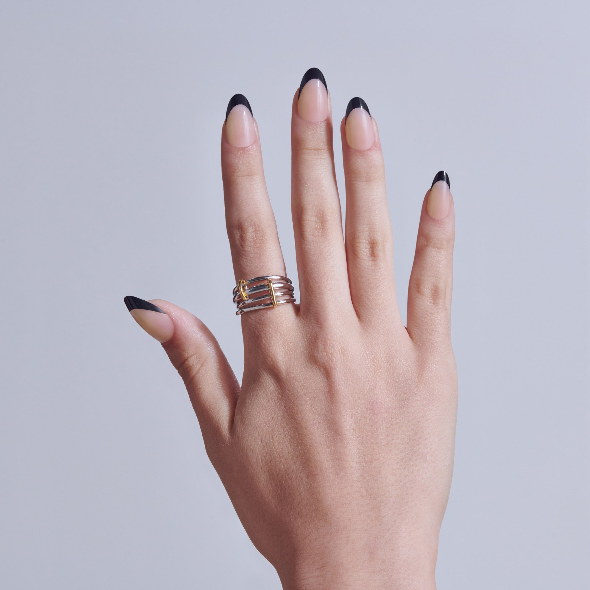 Hand displaying black-tipped almond nails with gold striped ring against gray background.