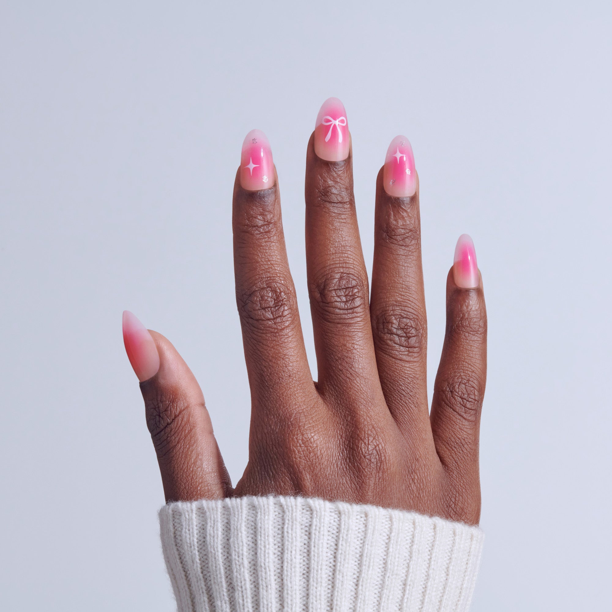 Hand with pink ombre nails featuring bow and star nail art designs