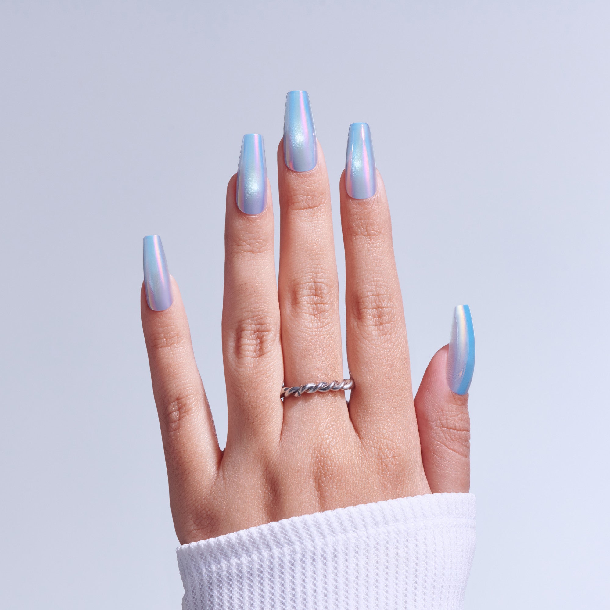Hand displaying iridescent blue ombre gel nails with twisted metal ring against white background.