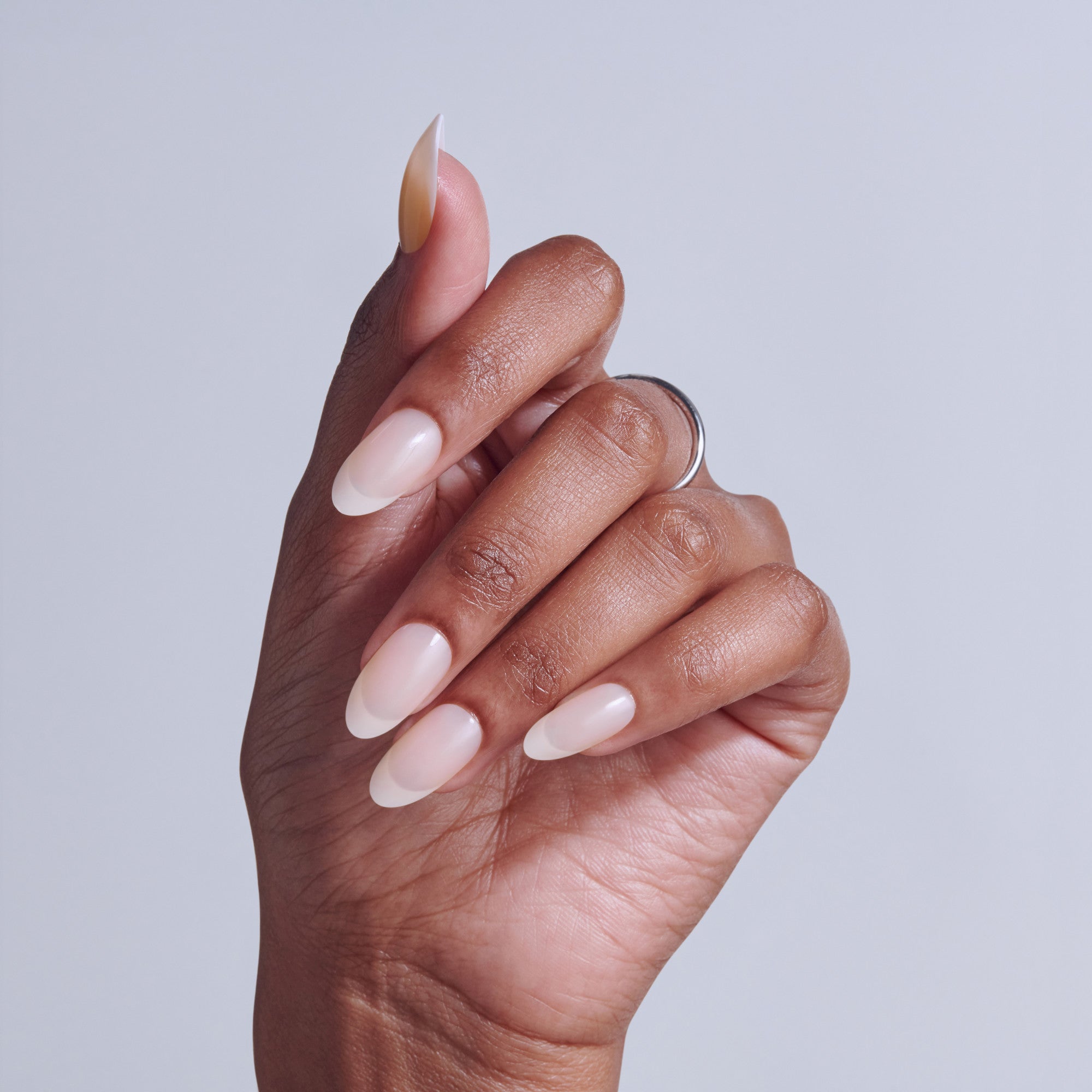 Hand with almond-shaped nails featuring white and pink ombre nail art design.
