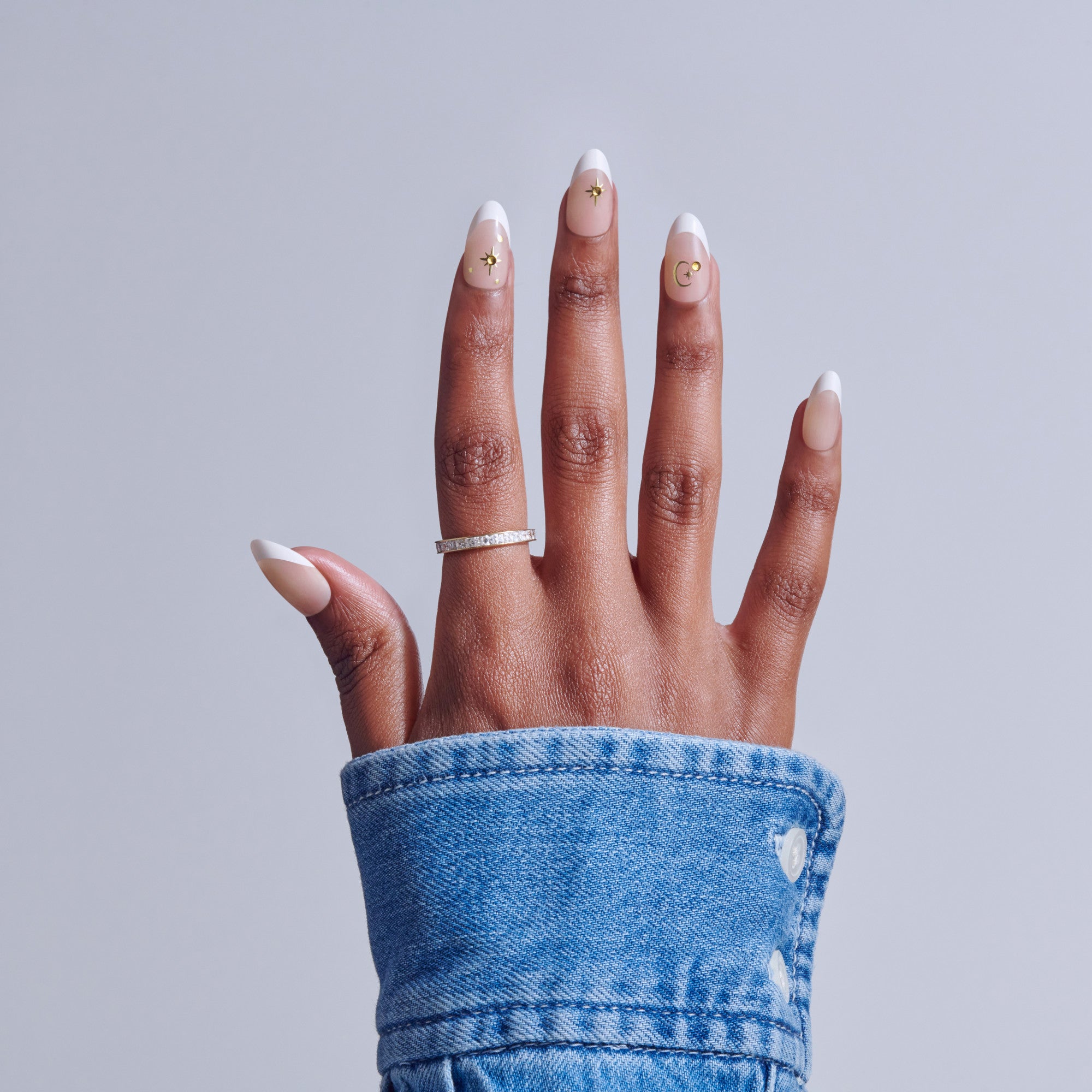 Hand with white French tip nails, gold accents, and diamond ring on blue denim sleeve.