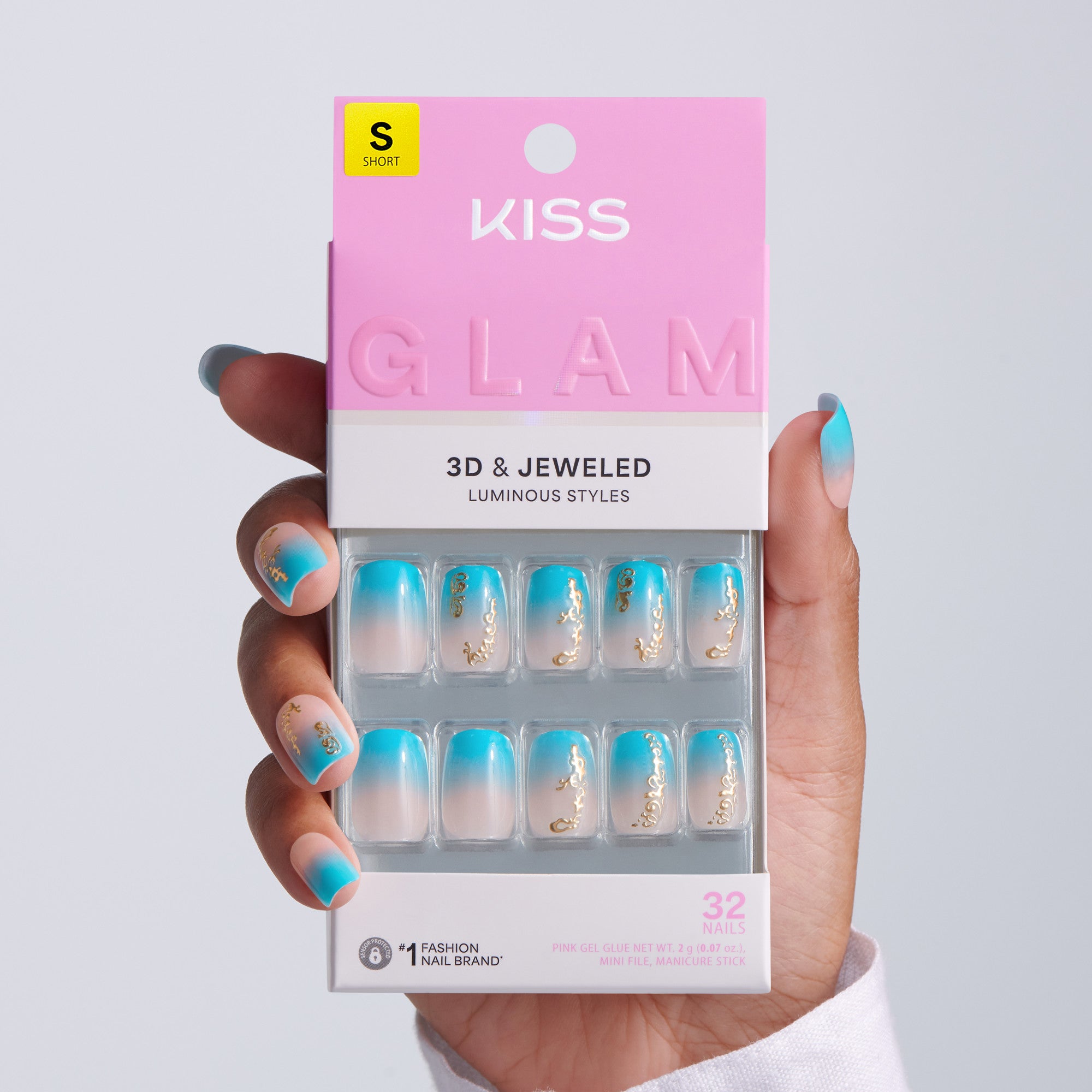 Hand holding KISS Glam 3D & Jeweled Luminous Styles press-on nails packaging, Short size, 32 nails, teal ombre squoval nails with gold chain accents on light gray background