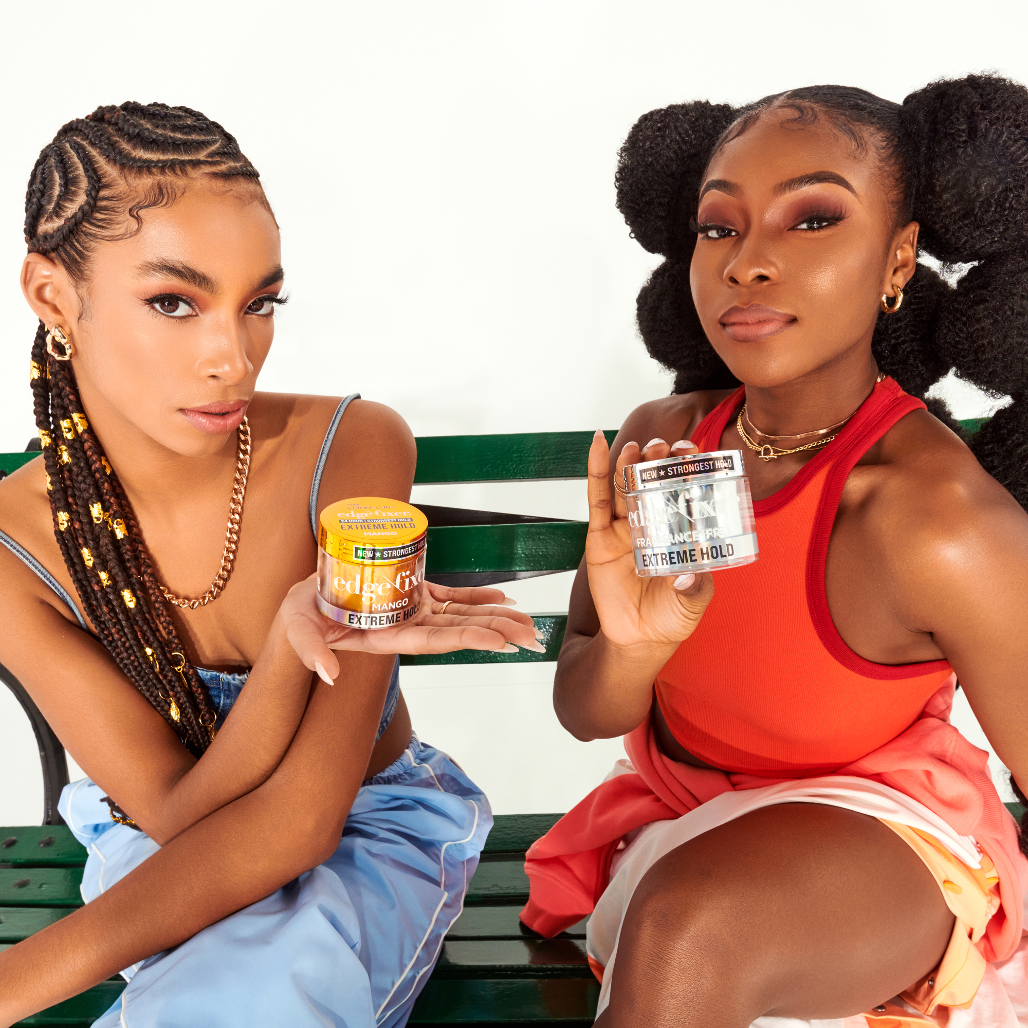 Two women sitting on a green bench holding KISS Edge Fixer Extreme Hold Gel jars; one mango-scented with bright orange lid, labeled "New Strongest Hold."