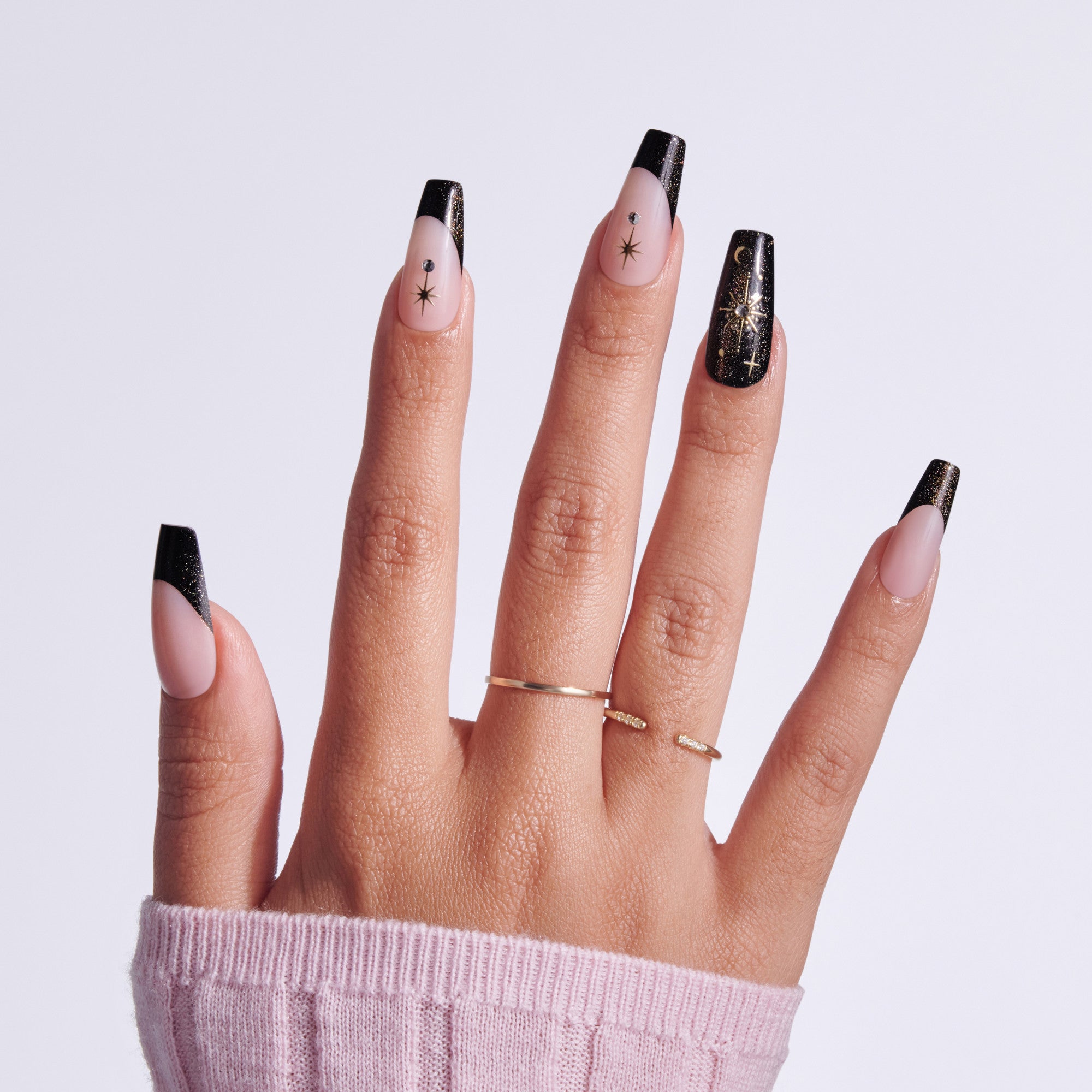 Black glitter coffin nails with star designs on natural nail beds, gold rings, pink sleeve visible.