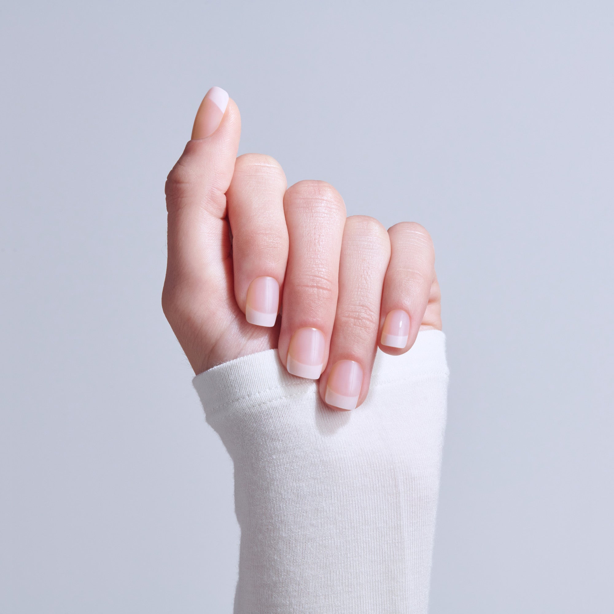 Hand with natural French manicure nails against light gray background
