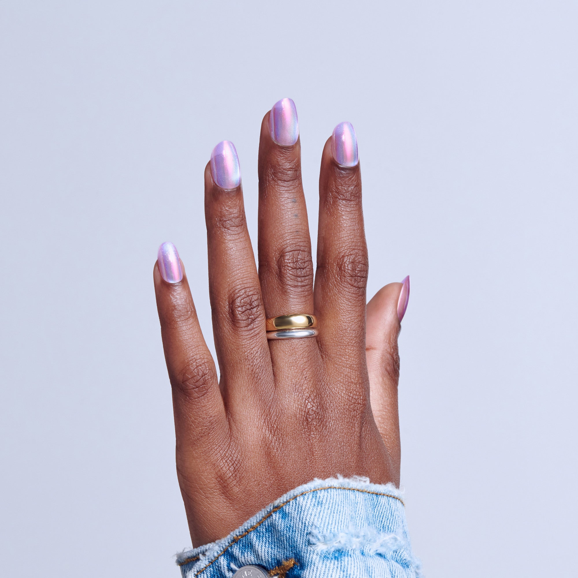 Hand with iridescent pink nail polish and gold ring against light blue background