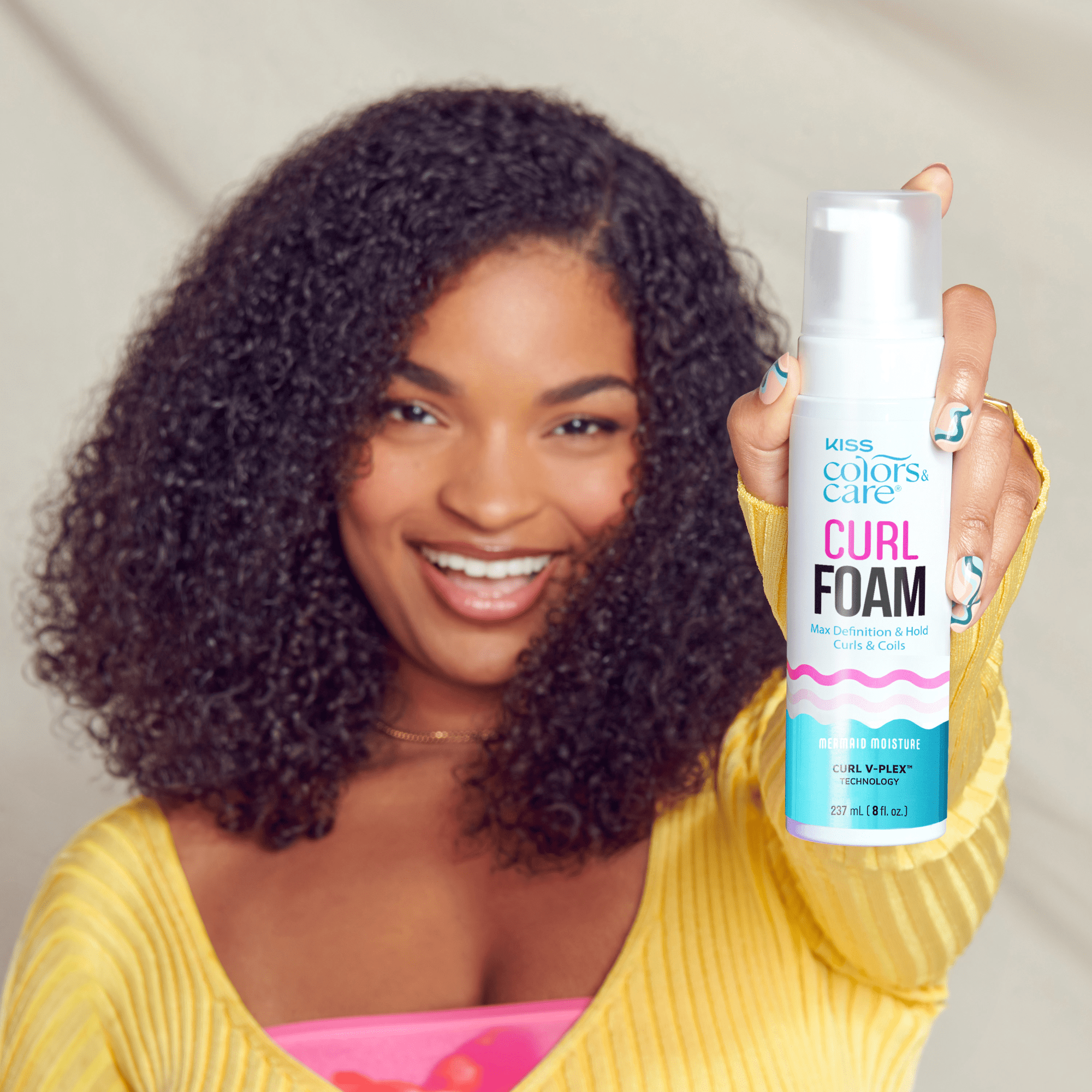 Woman holding KISS Colors & Care Curl Foam bottle, showcasing defined curls.