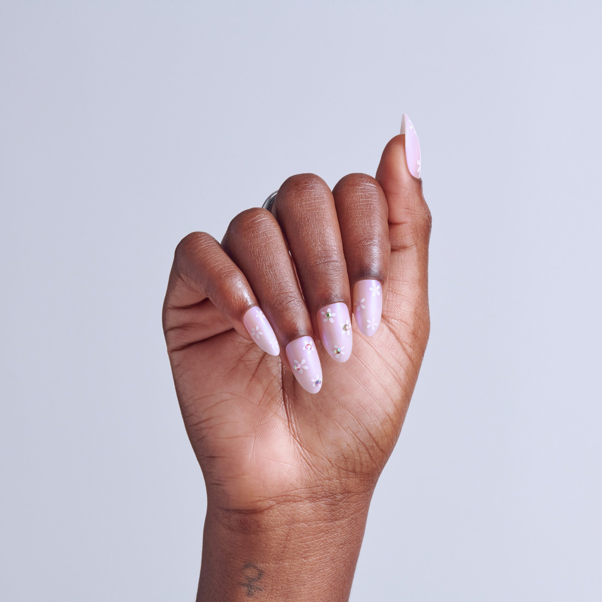 Hand displaying long almond nails with pink polish and rhinestone accents against white background.