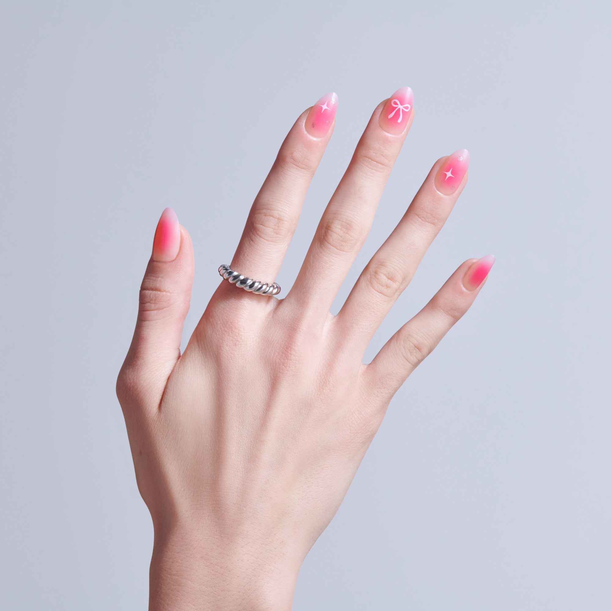 Hand with pink ombre nails featuring star and bow designs, wearing silver ring.