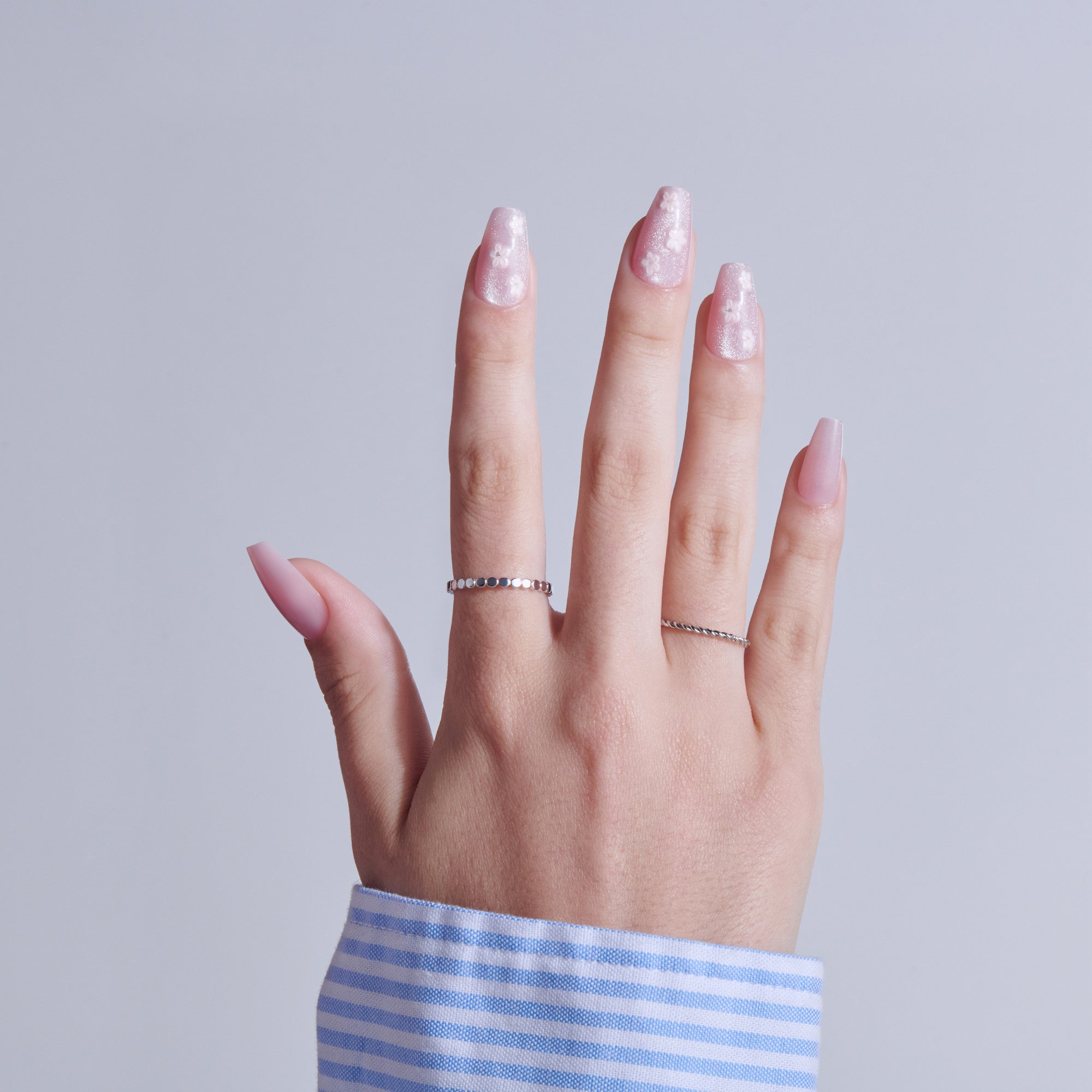 Hand with pink glitter nails and silver rings against white background