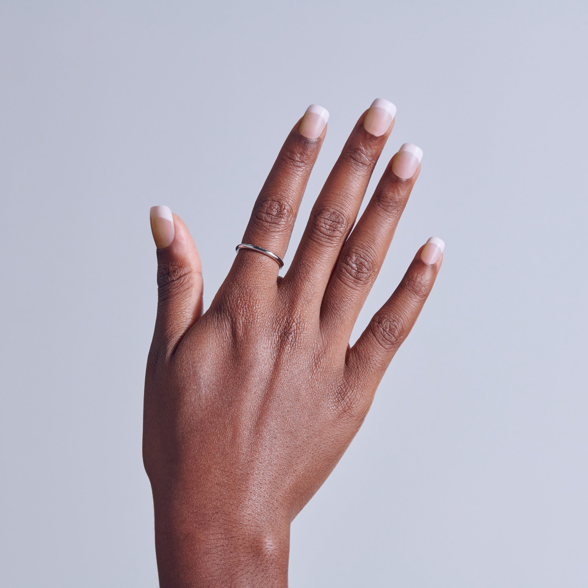Hand with natural nails and white French manicure against gray background