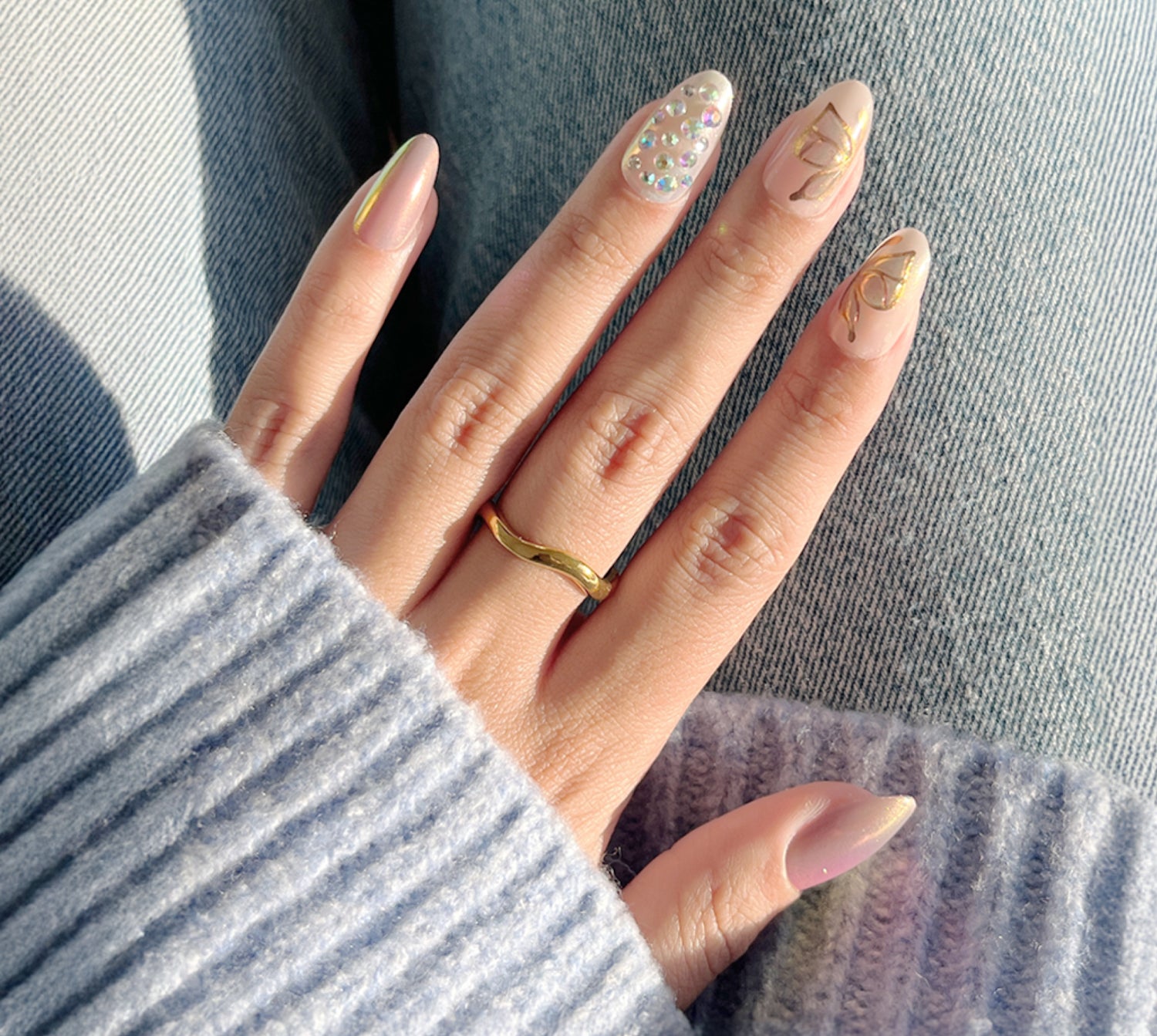 Manicured hands with almond nails featuring gold accents, rhinestones, and minimalist designs.