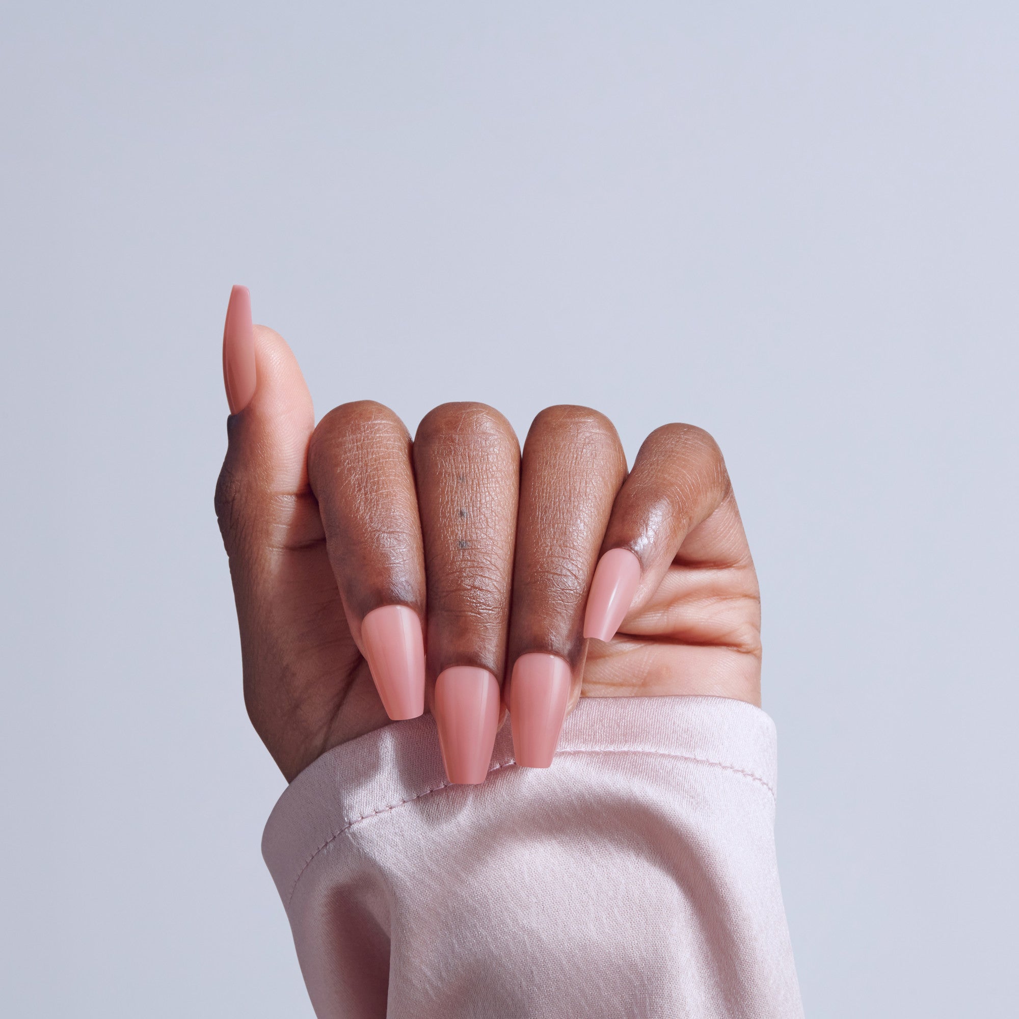 Hand with pink acrylic nails in coffin shape against light blue background