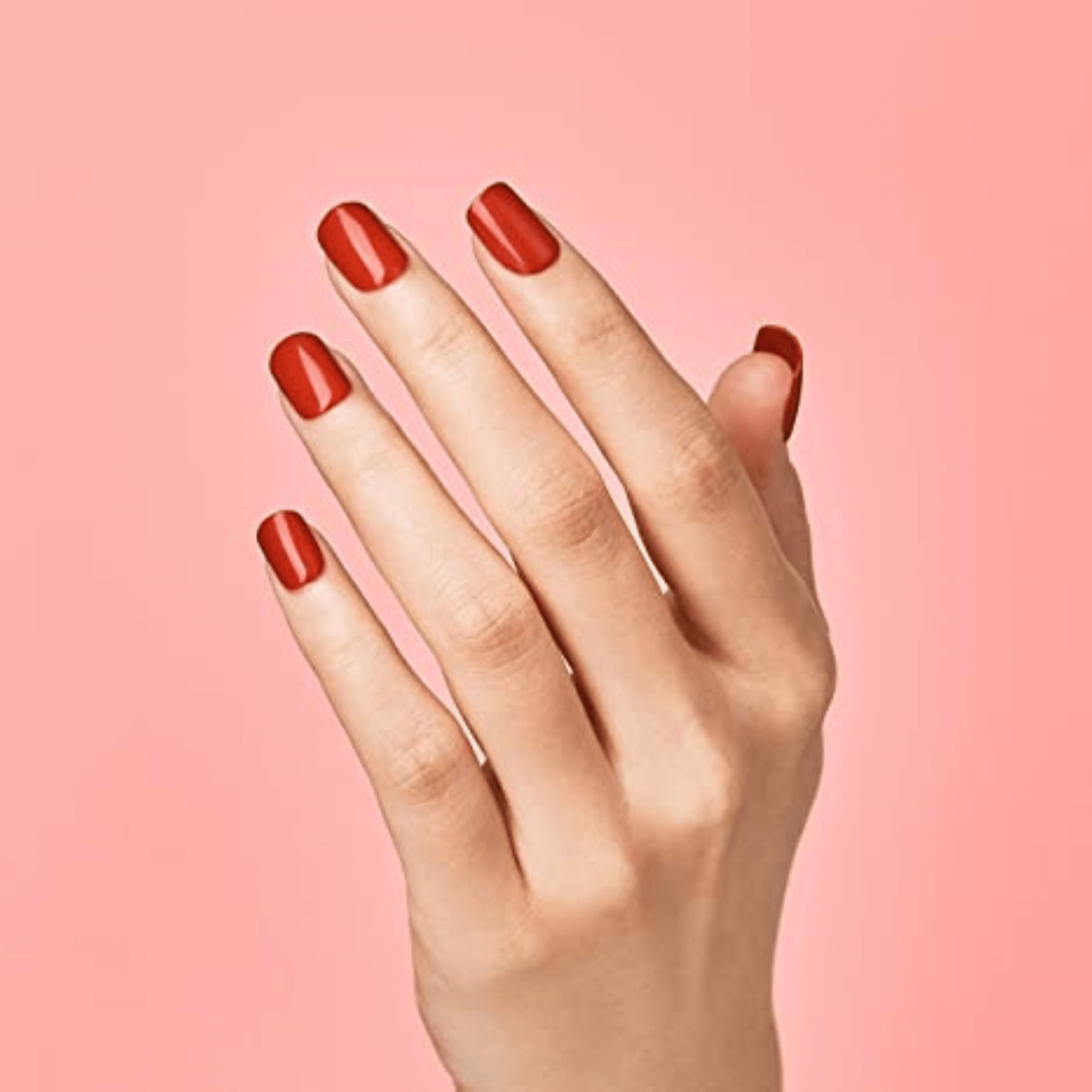 Hand with glossy, medium-length red press-on nails against a solid pink background, showing the \