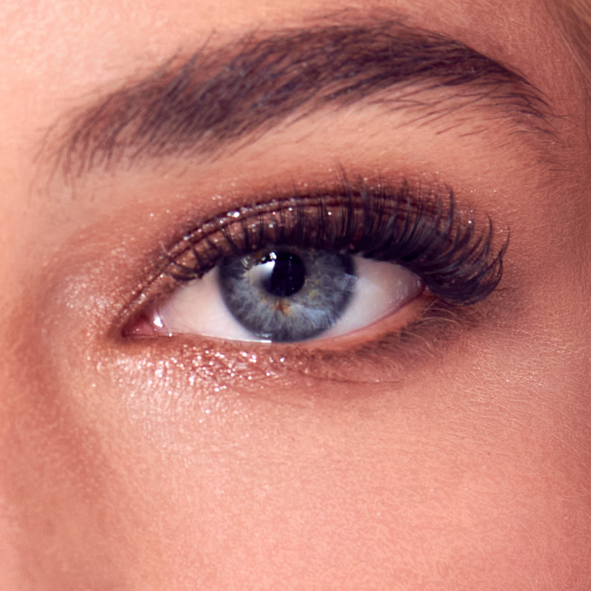 Close-up of eye with blue iris, dark eyebrow, and sparkly bronze eyeshadow with mascara.