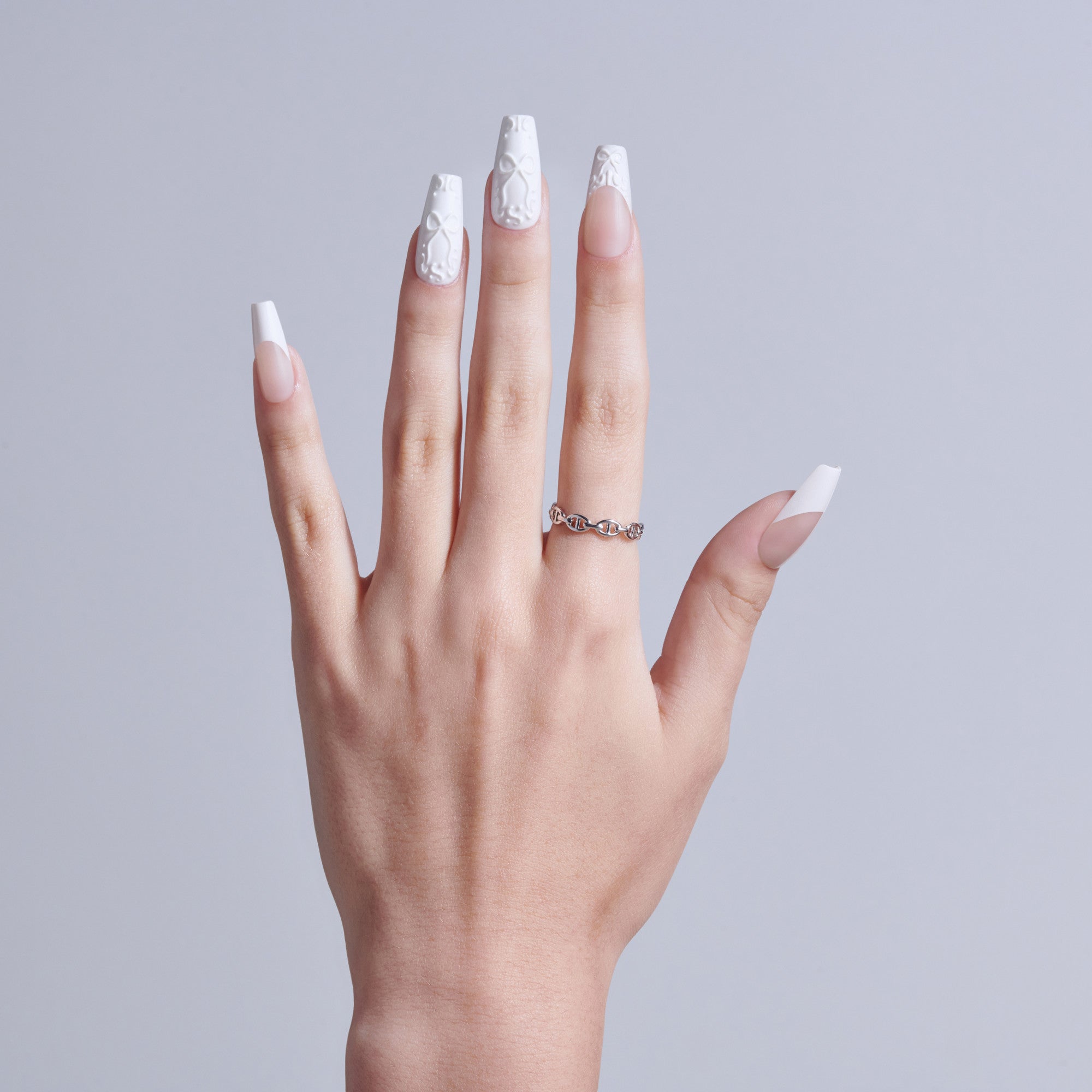 Hand displaying white French tip nails with lace design and decorative ring.