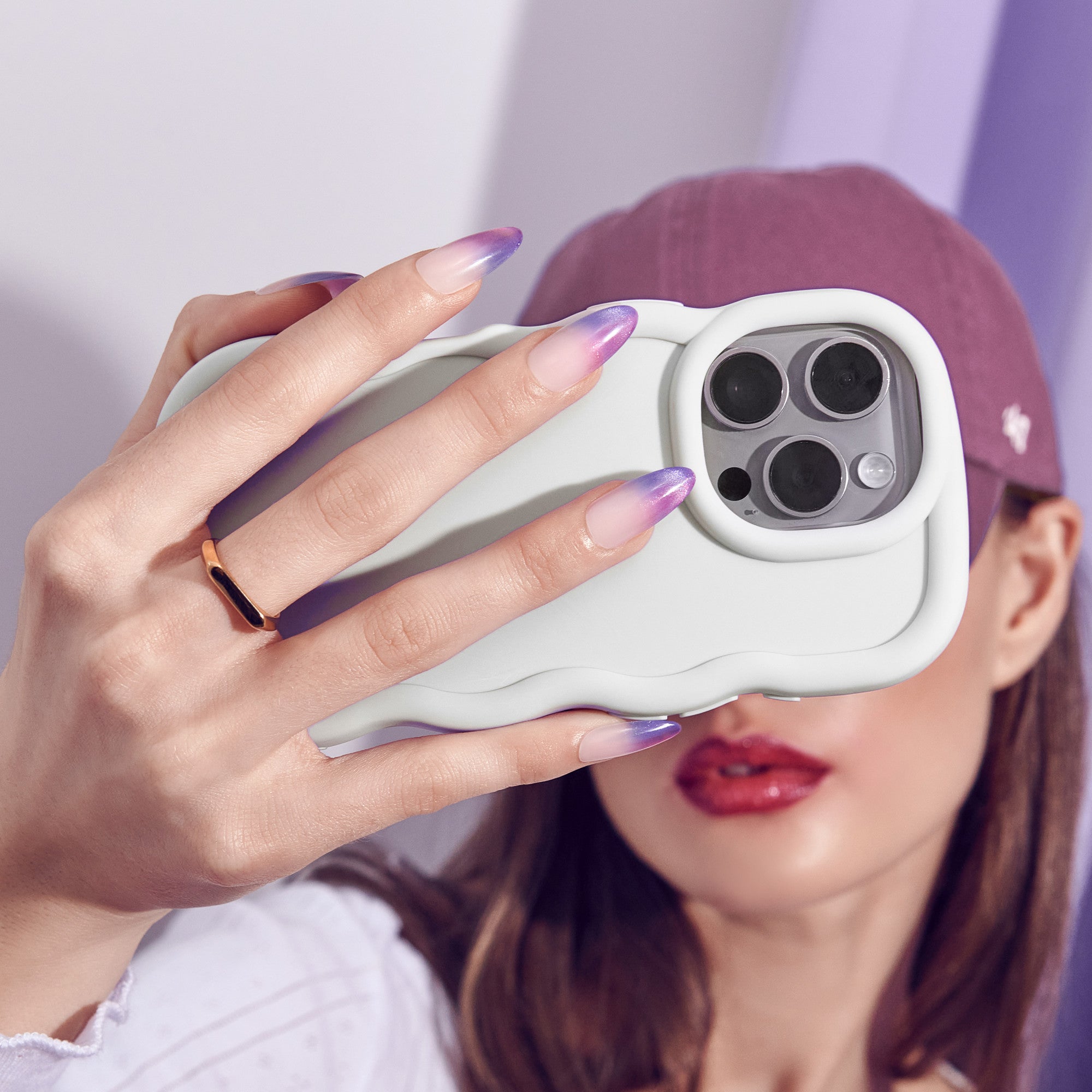 Person holding white iPhone 14 Pro with purple ombre nails and gold ring