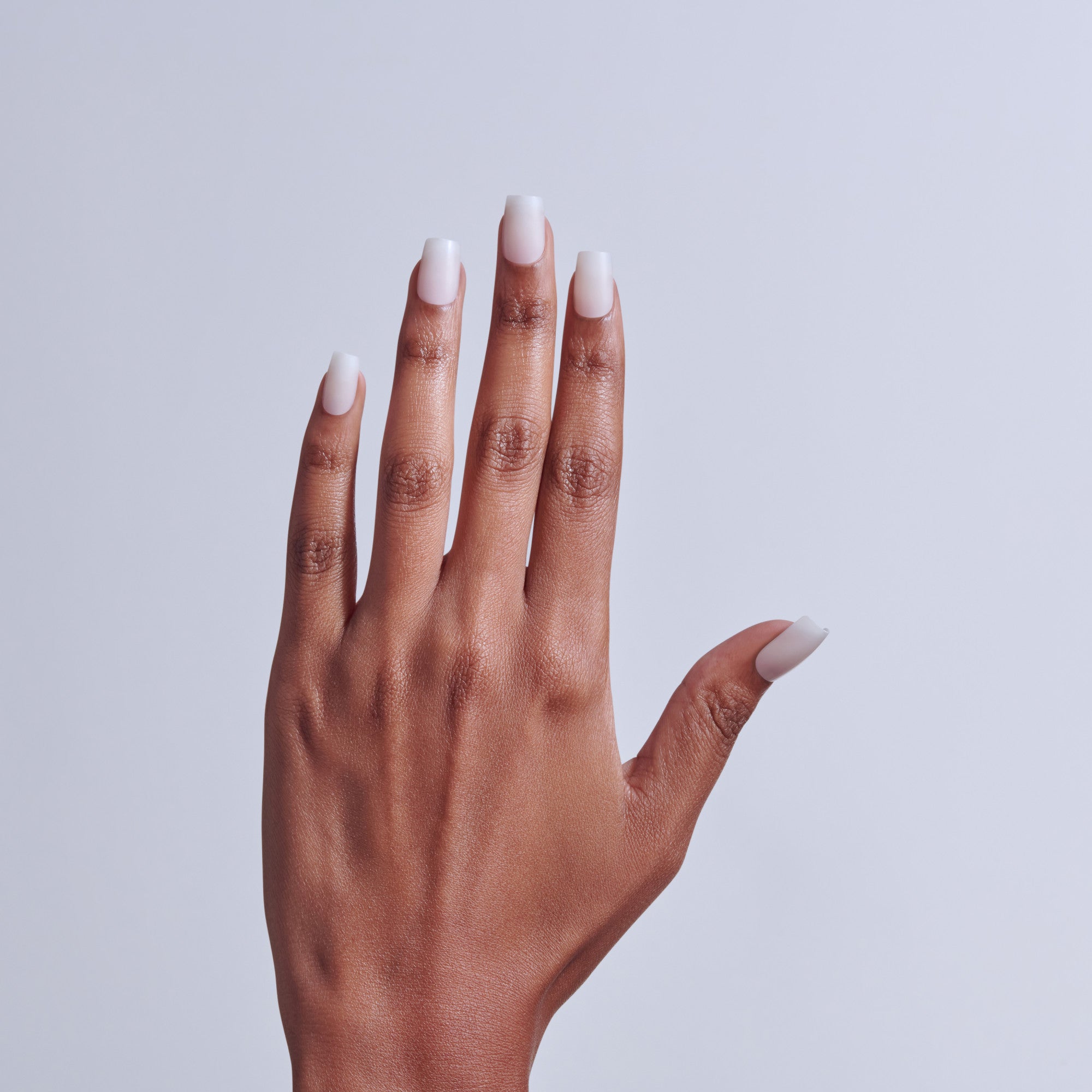 Hand with white ombré nail manicure against light gray background.