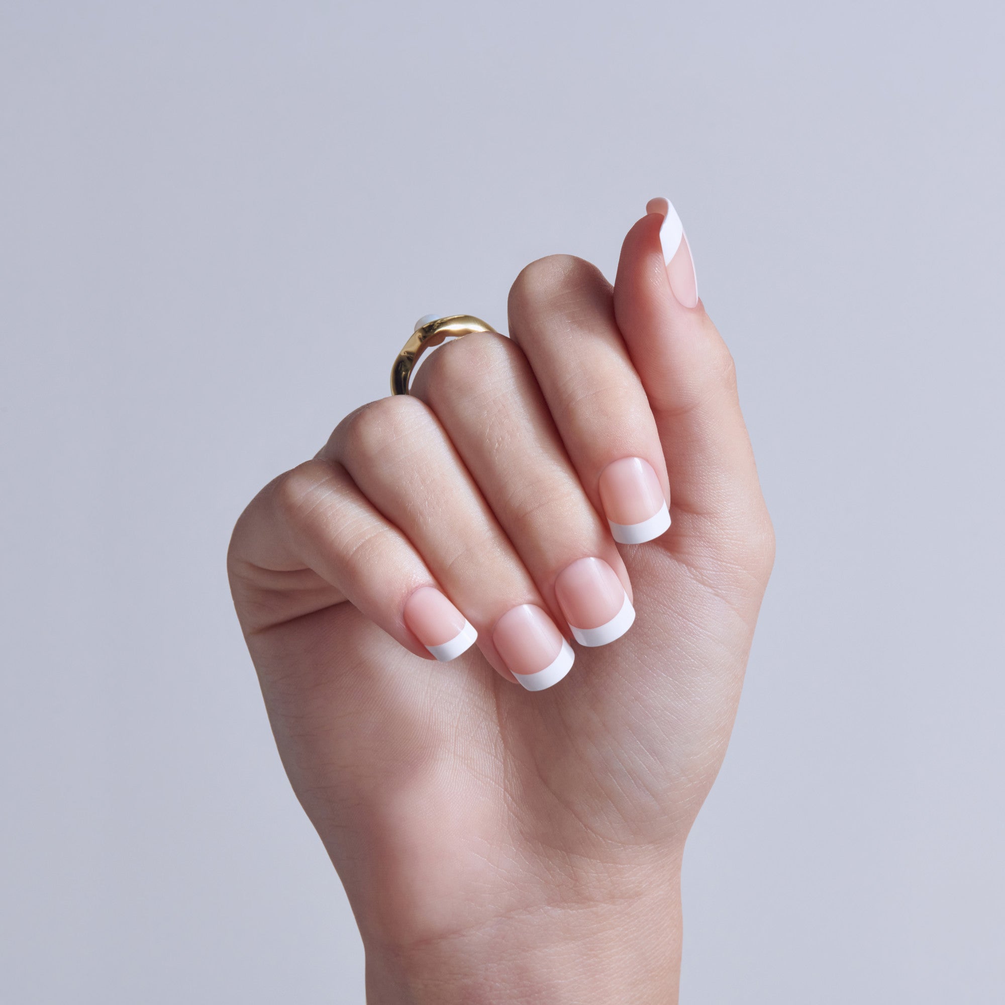 Hand displaying French manicure nails with white tips and gold ring against light gray background.