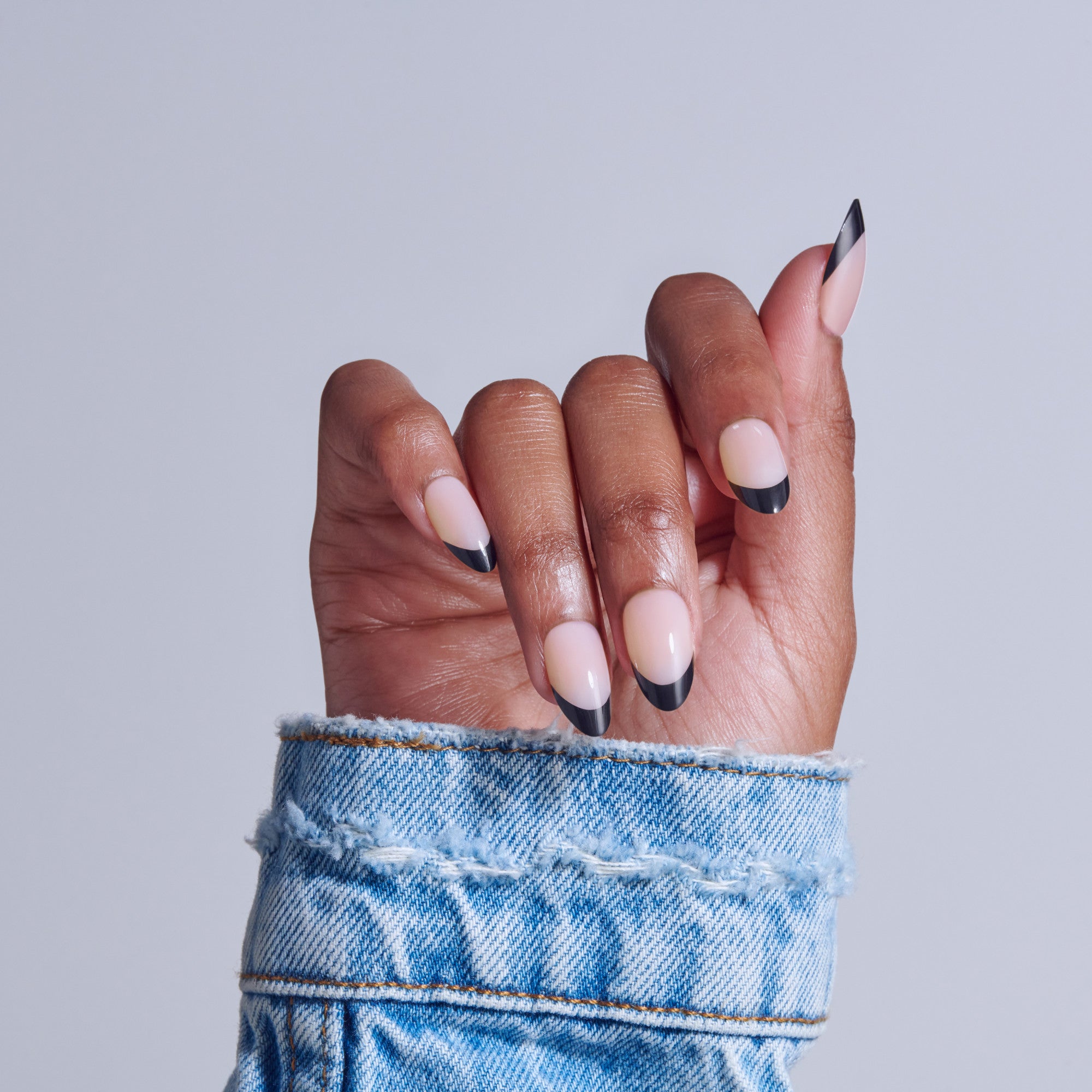 Hand with black and white ombre nails wearing distressed blue denim cuff.