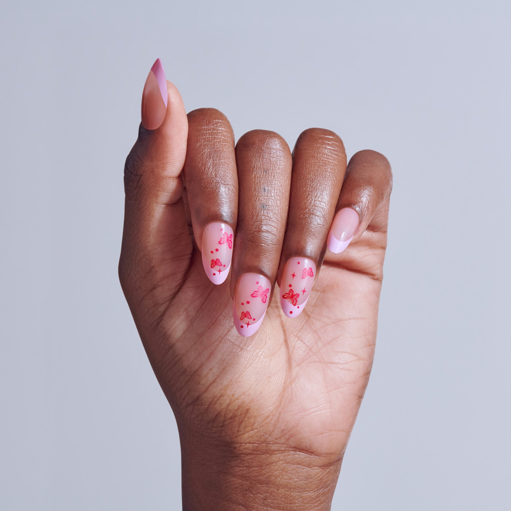 Hand displaying almond-shaped nails with pink base and red butterfly designs.