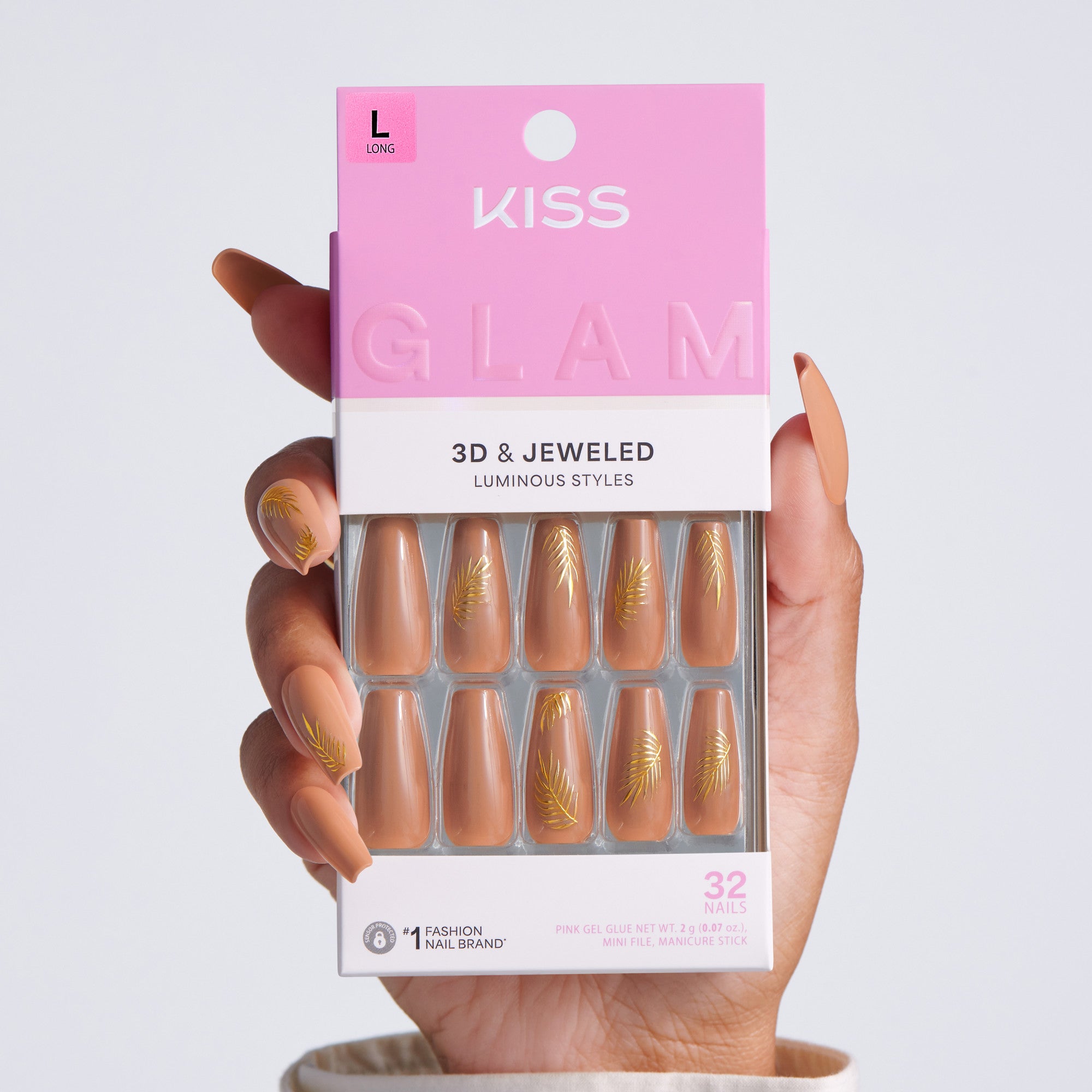 Hand holding KISS Glam 3D & Jeweled Luminous Styles press-on nails packaging, Long size, 32 nails, pink box showing nude nails with gold leaf accents through clear window