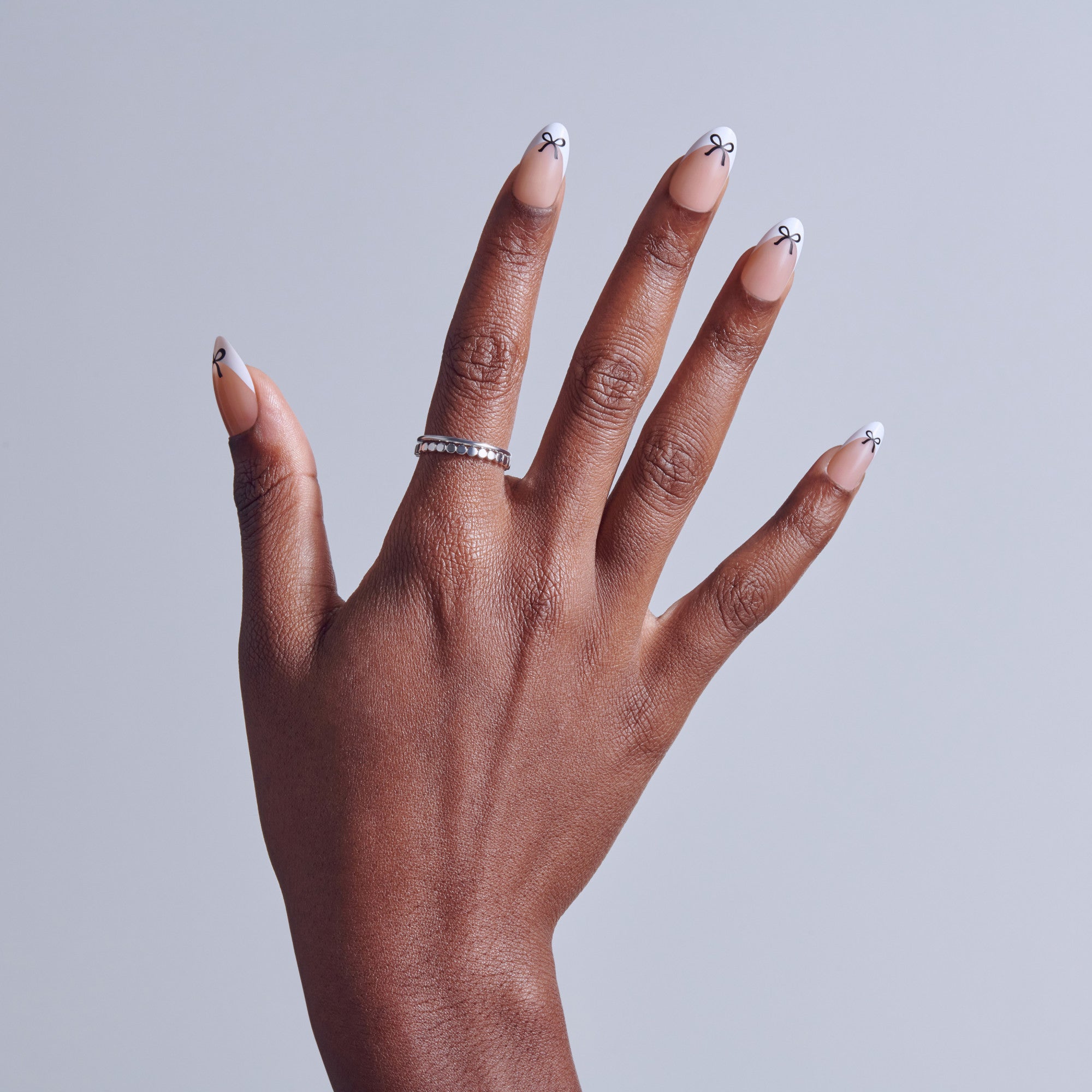 Hand with white French tip manicure and small anchor nail art designs, wearing diamond ring.