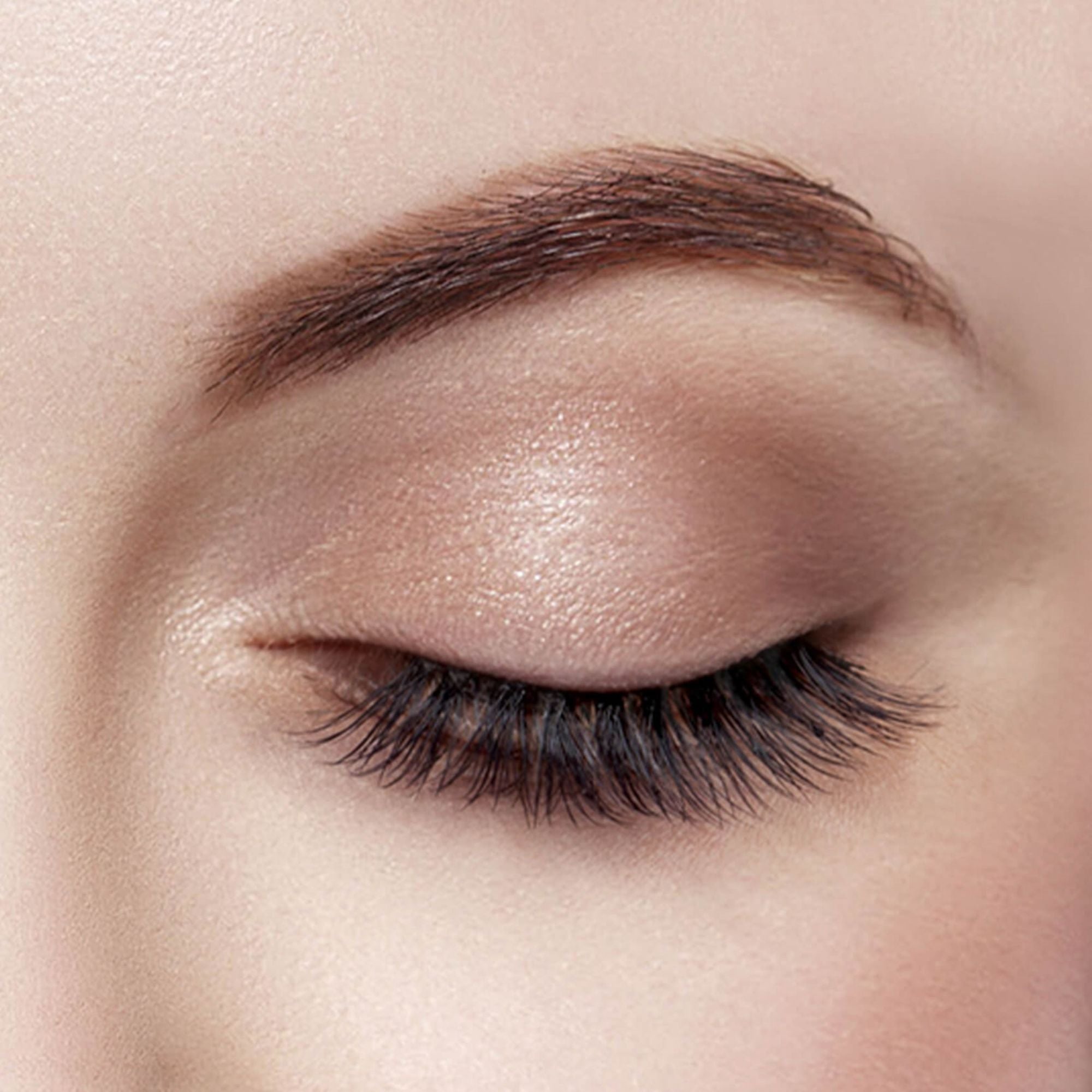 Close-up of a closed eye with long, full, and dark faux lash extensions enhancing the natural lashes and an arched, well-groomed eyebrow.