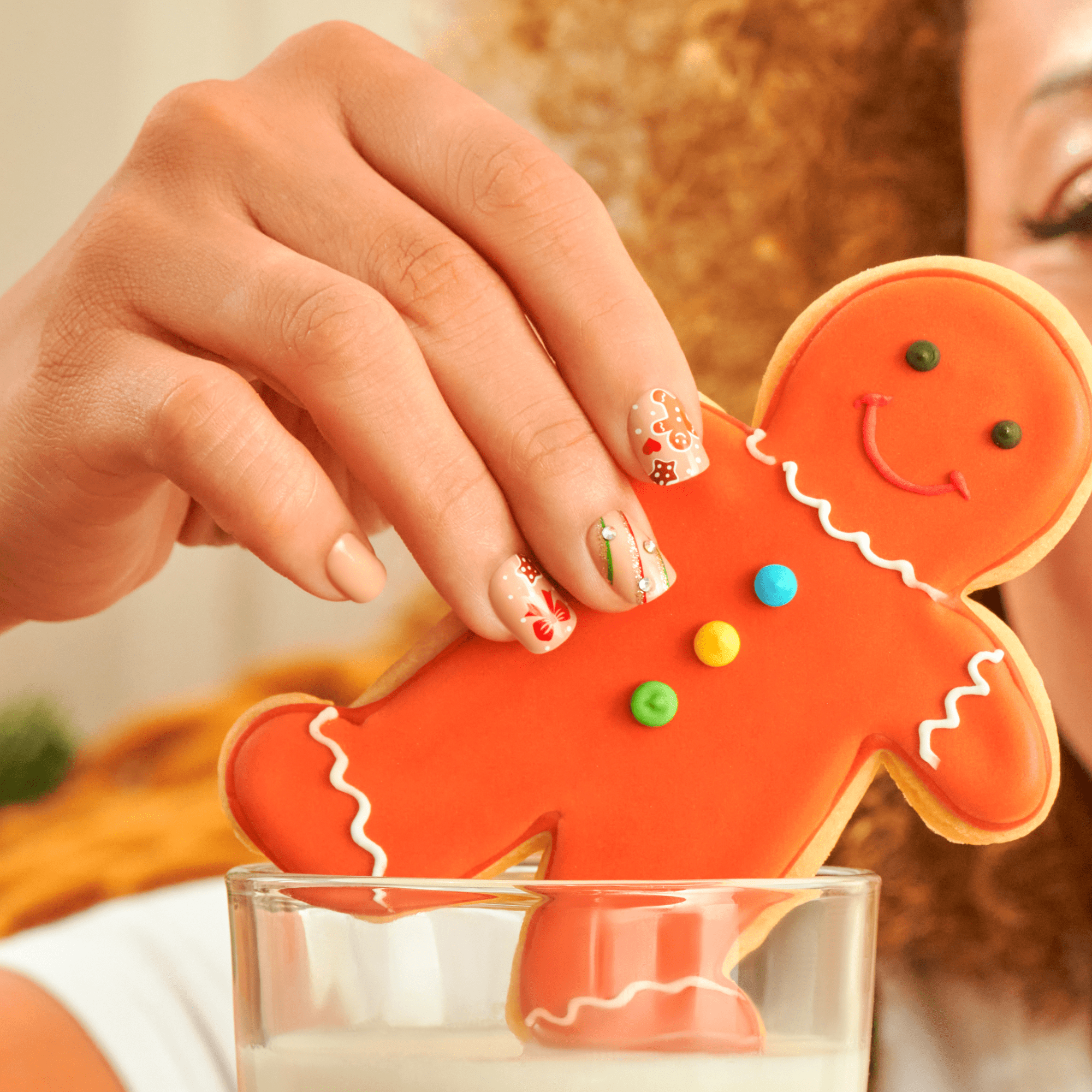 Hand holding decorated gingerbread man cookie over milk glass, festive holiday nail art visible.