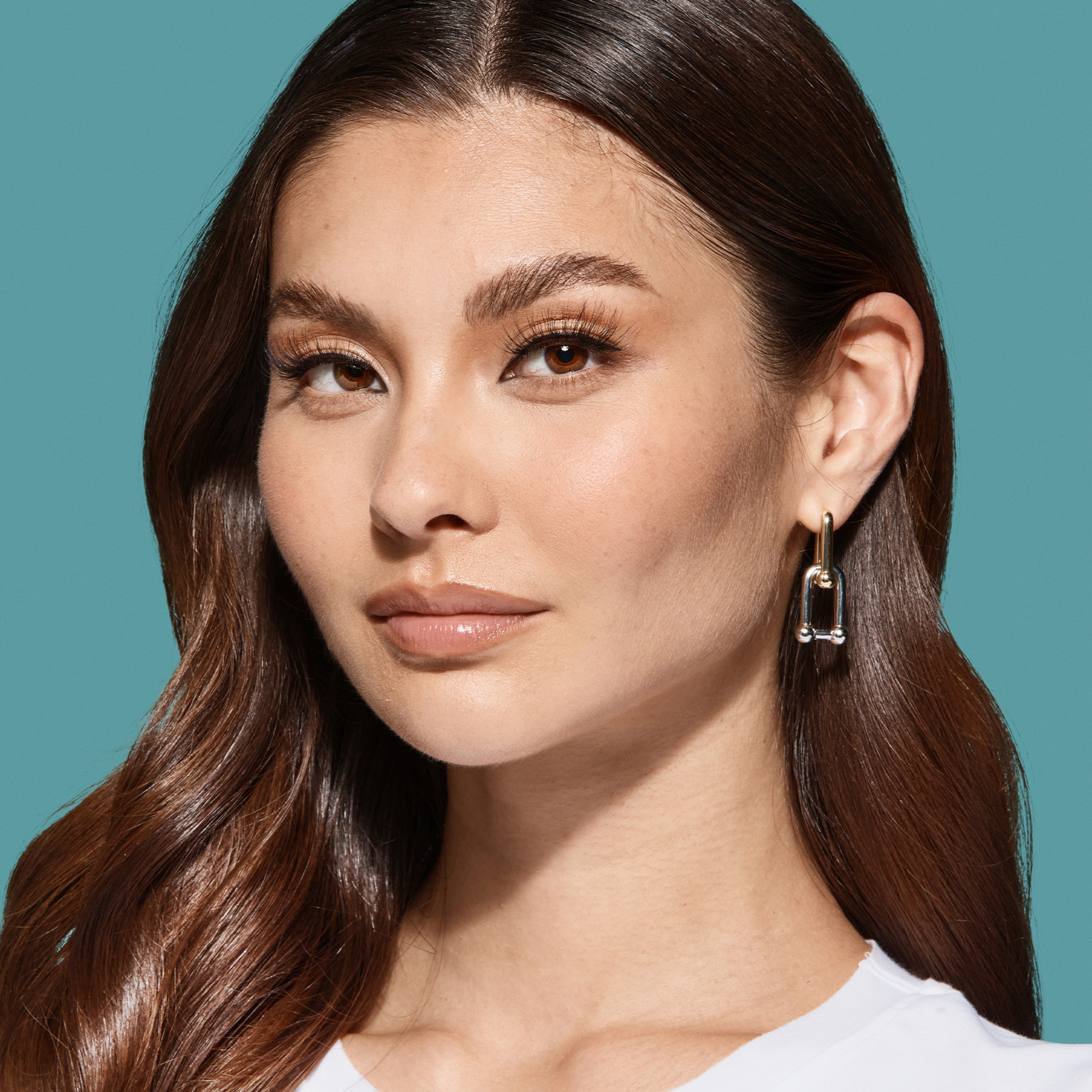 Close-up of a woman with smooth, glossy brown hair and natural makeup, showcasing long, full lashes against a teal background.