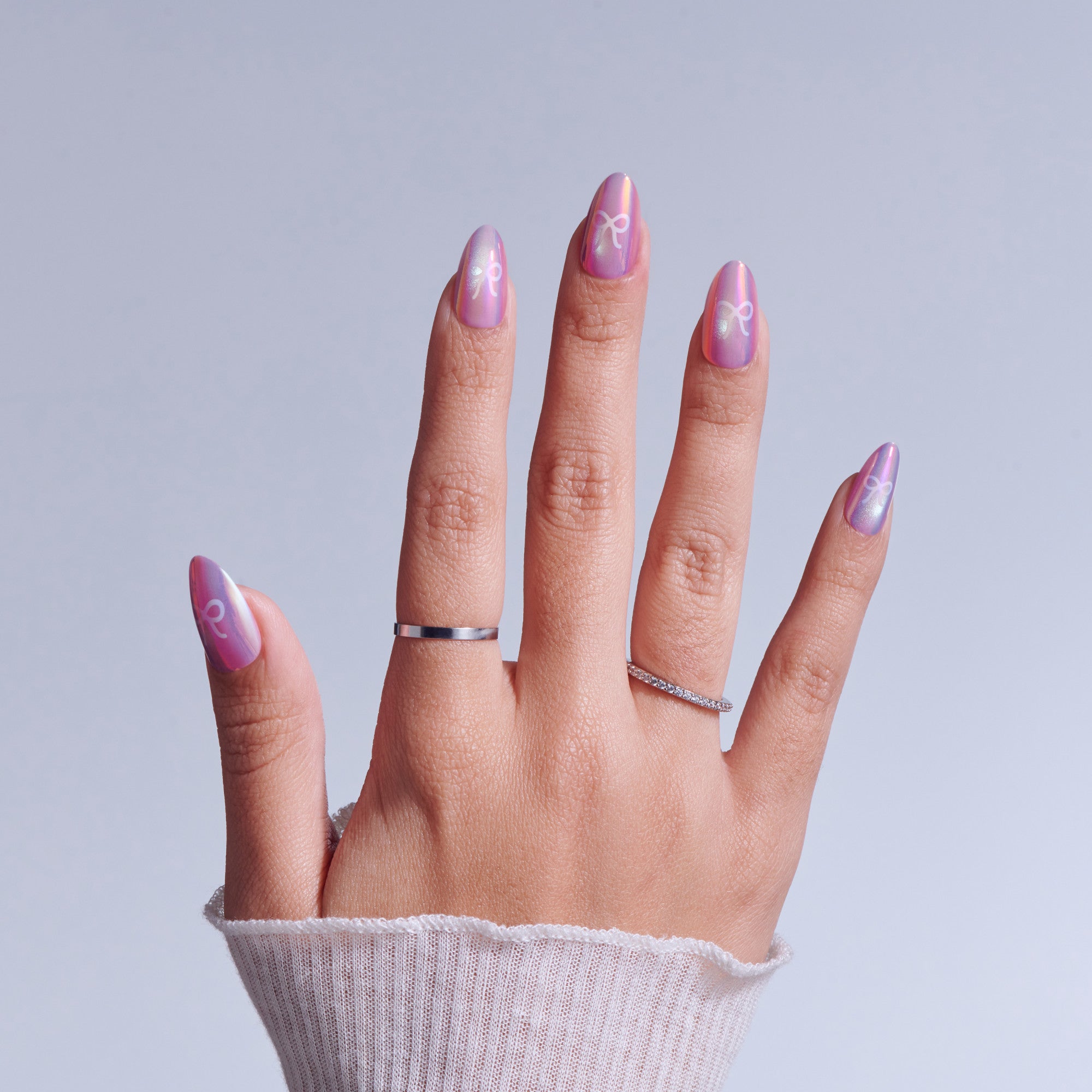 Hand with pink ombre nails featuring white symbol designs and silver rings against light background
