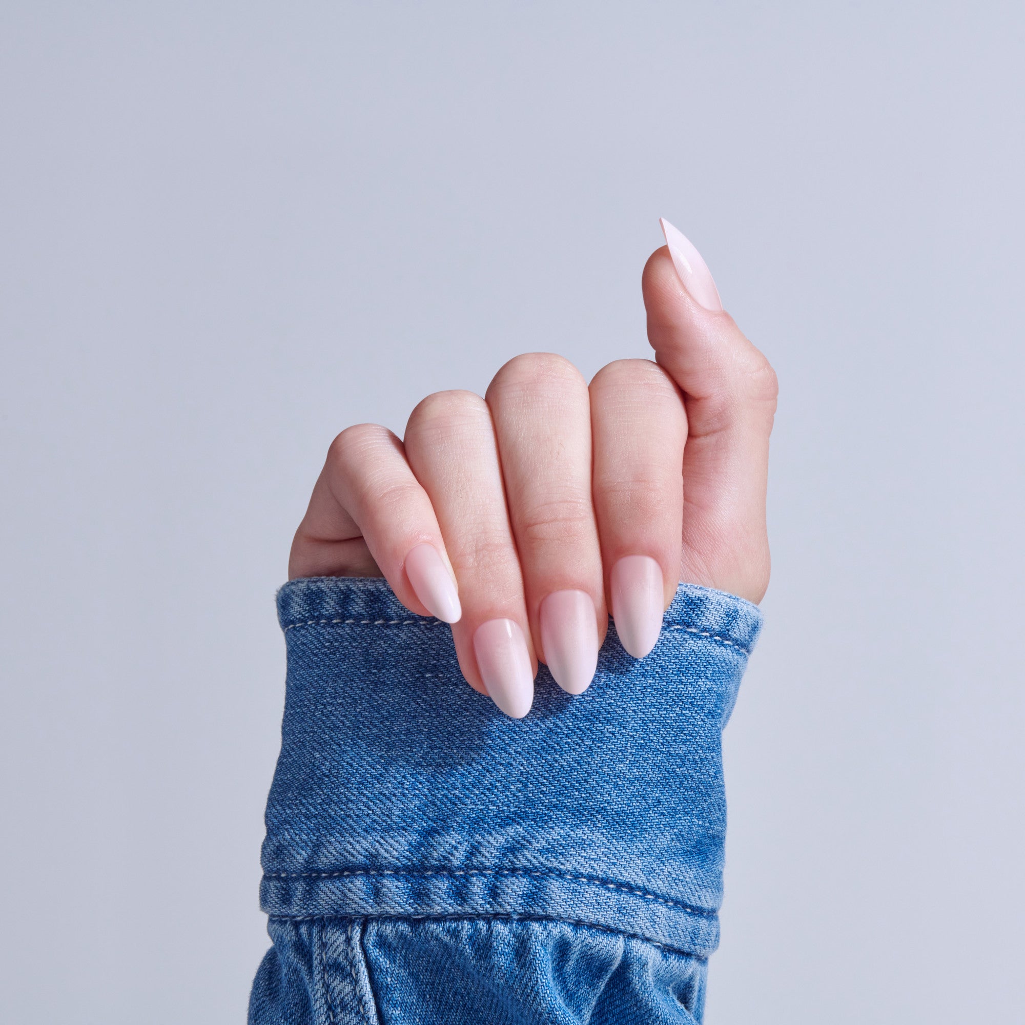 Hand with almond-shaped acrylic nails in pink ombre, wearing blue denim cuff against gray background.