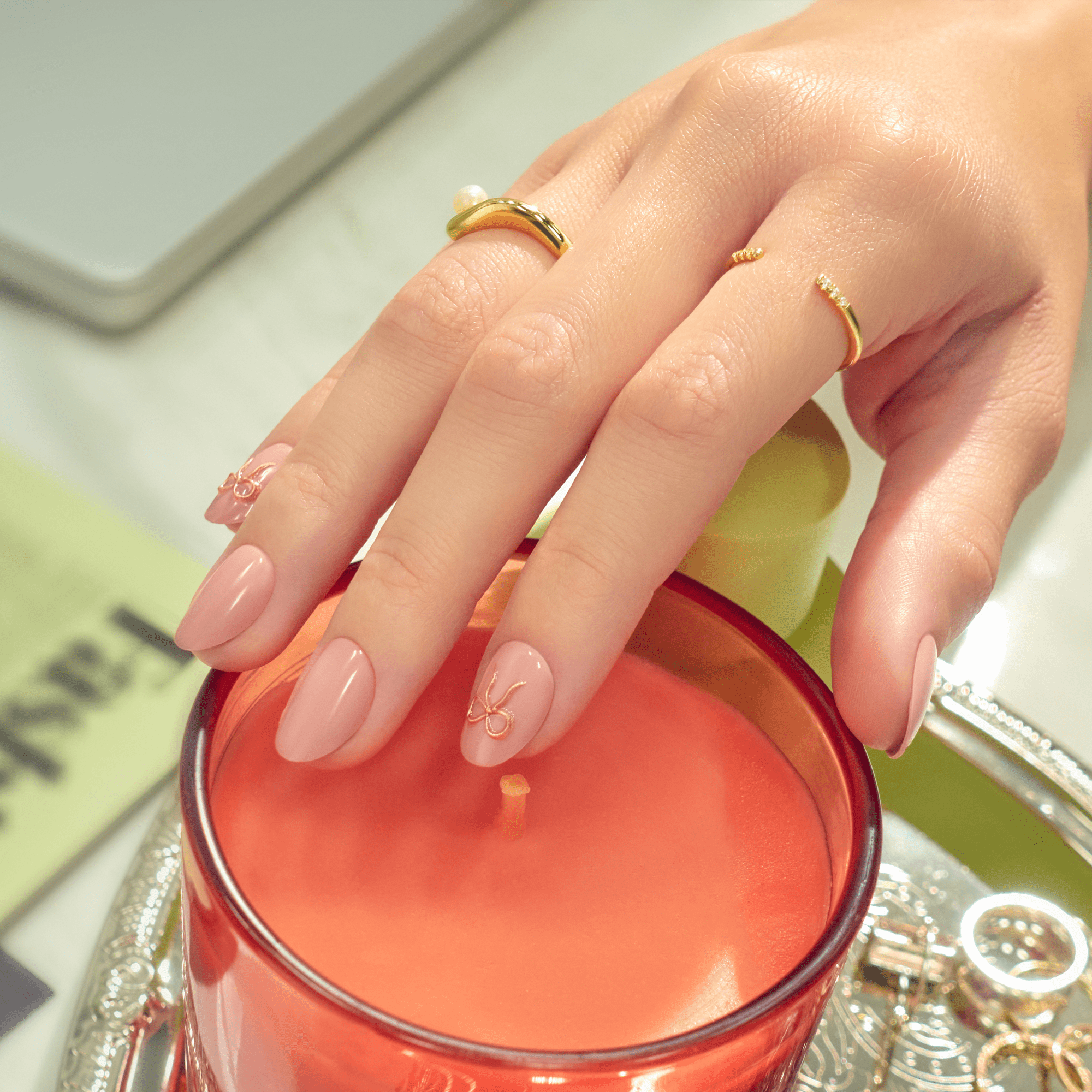 Manicured hands with pink nails and gold rings over red candle