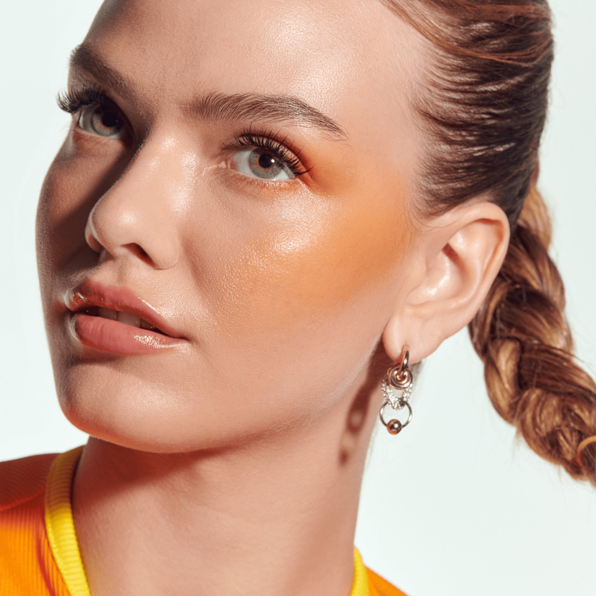 Close-up of a woman with a sun-kissed glow on her face, wearing an orange top.