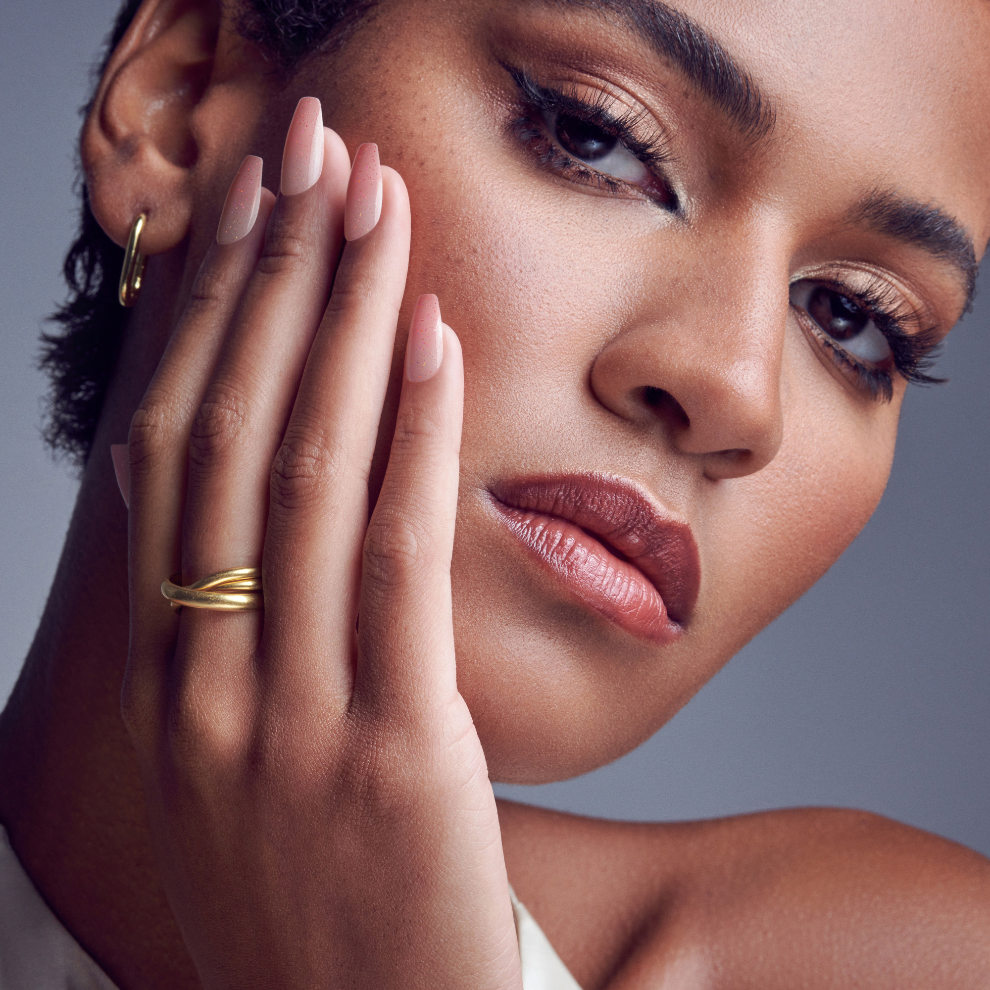 Close-up of a woman with medium skin tone wearing long, soft pink press-on gel nails with subtle glitter, showcasing a natural, elegant manicure.
