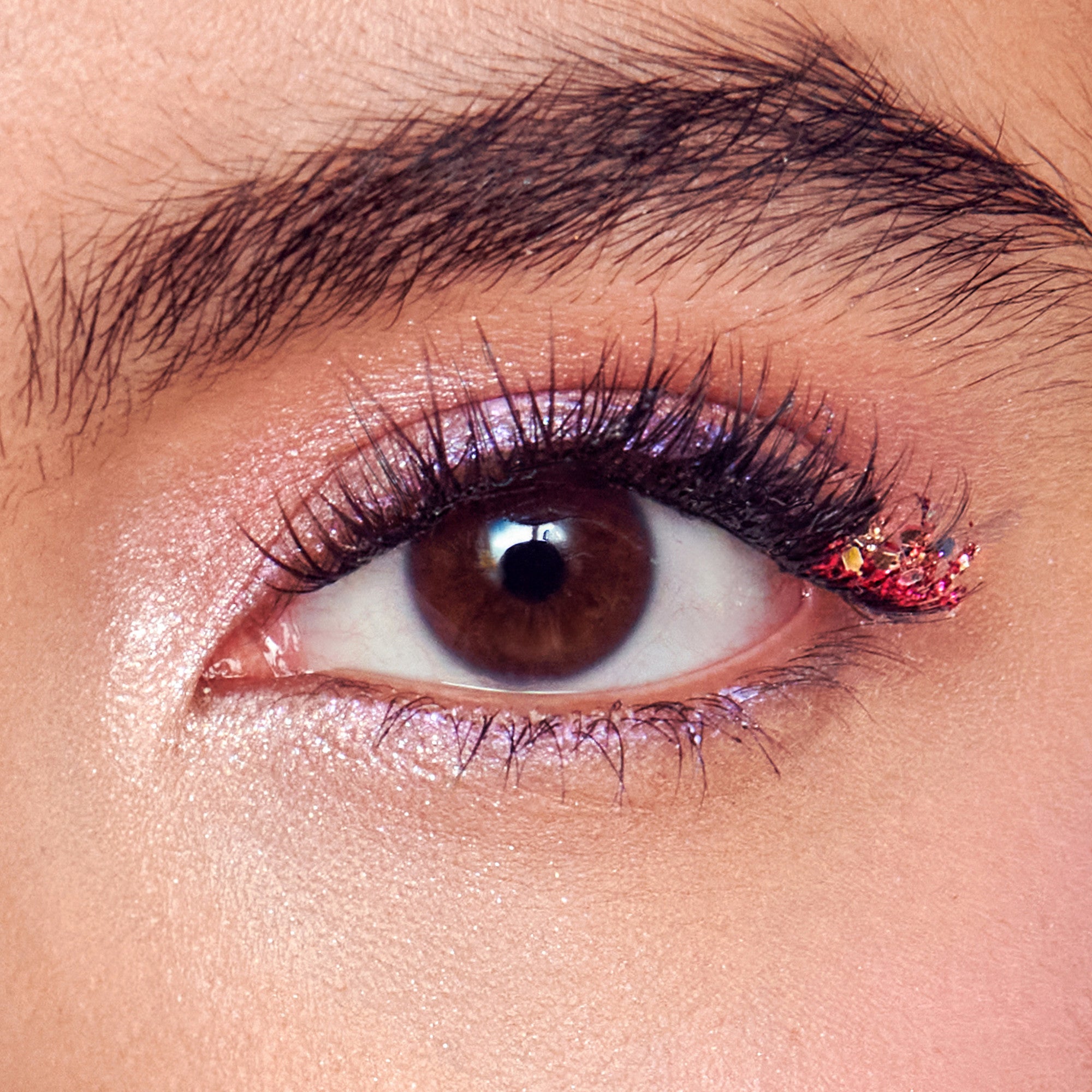 Close-up of eye with brown iris, black winged eyeliner, dark mascara, and gold glitter on lower lash line.