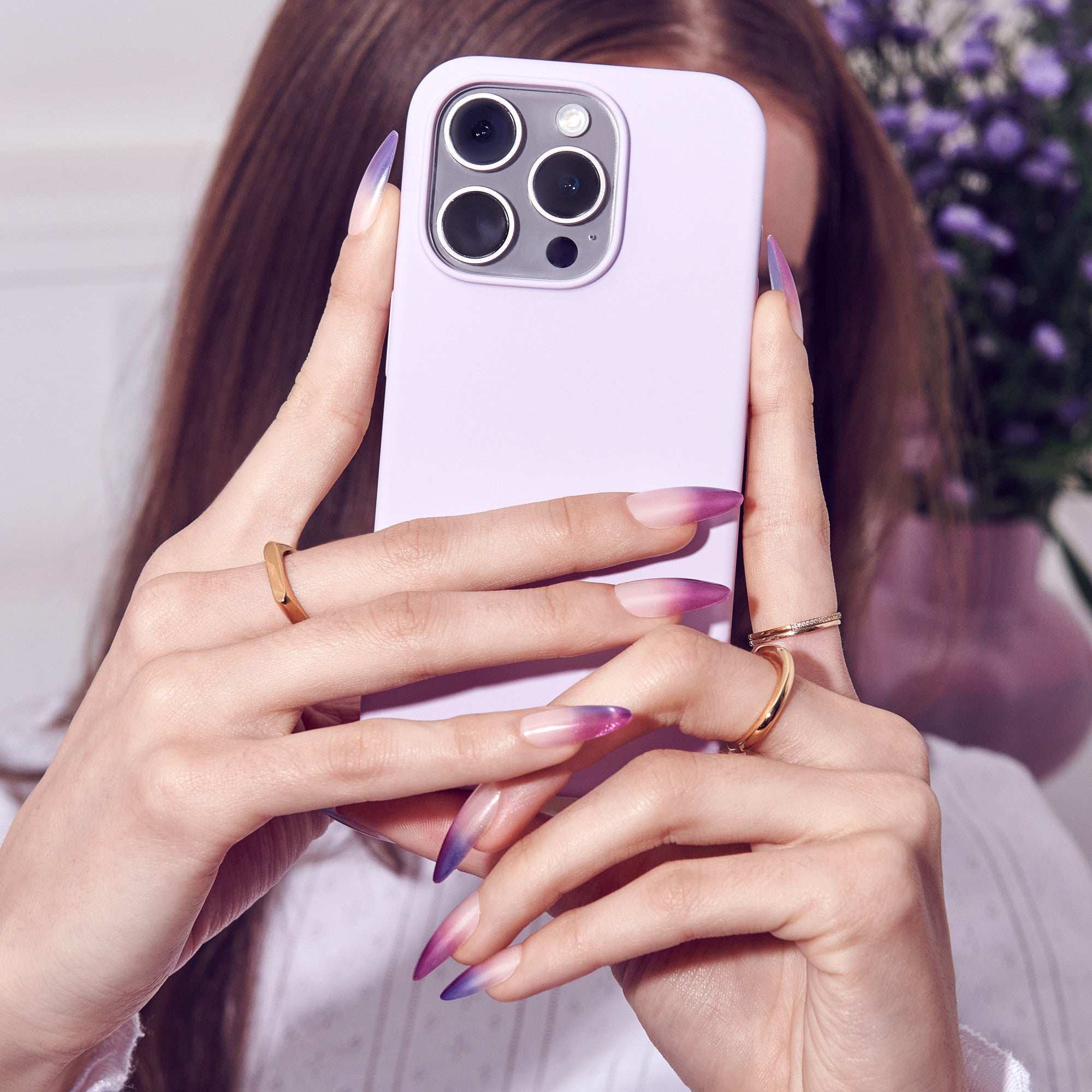 Woman holding lavender iPhone 14 Pro with purple ombre nails and gold rings