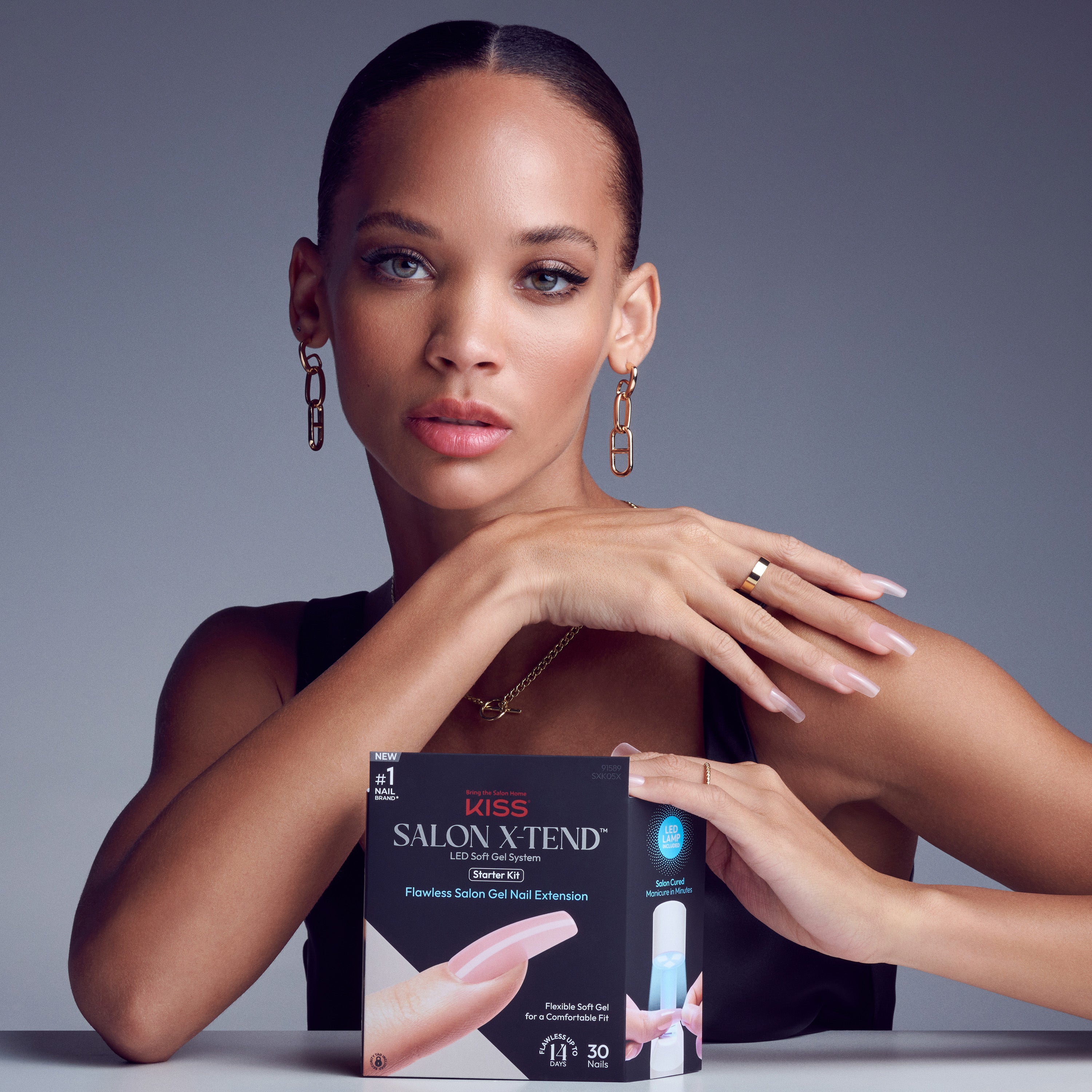 Woman with light pink gel nail extensions holds KISS Salon X-tend LED Soft Gel Starter Kit packaging featuring nail extension image and LED lamp icon.