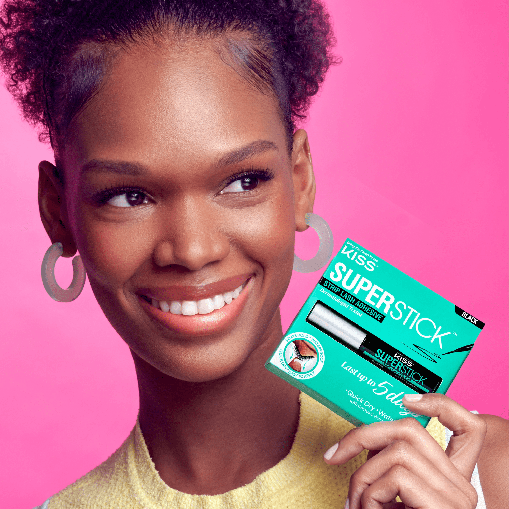 Woman holding Kiss SuperStick strip lash adhesive against pink background